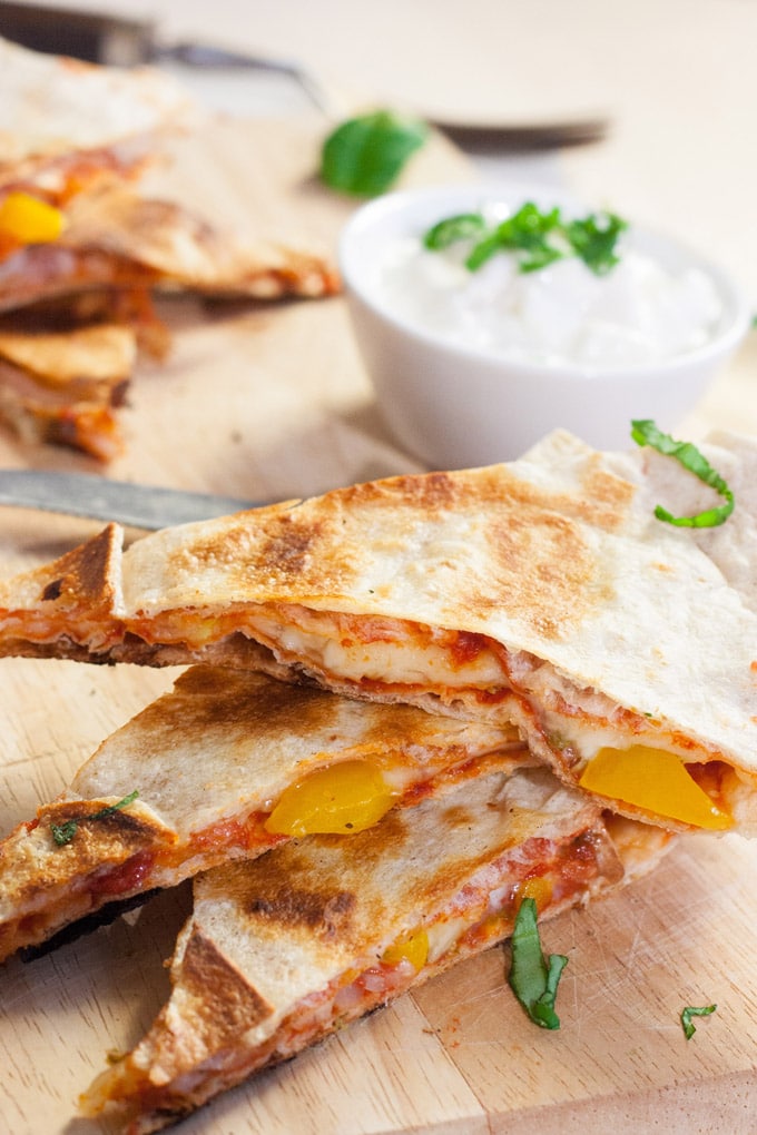 Pizzadillas auf einem Holzbrett. Im Hintergrund sieht man einen Joghurt-Dip.