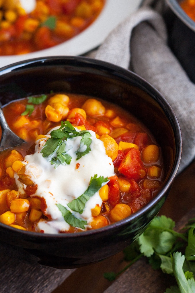 Zwei Portionen Kichererbsen-Stew mit Tomaten in einer schwarzen Schüssel, getoppt mit einem Klacks Naturjoghurt und Petersilie.