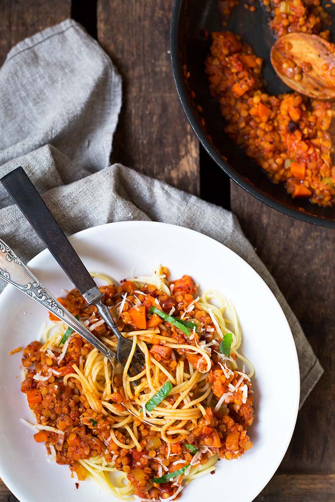 Ein Teller Spaghetti mit Roter Linsen-Bolognese und eine Pfanne gefüllt mit veganer Bolognese.