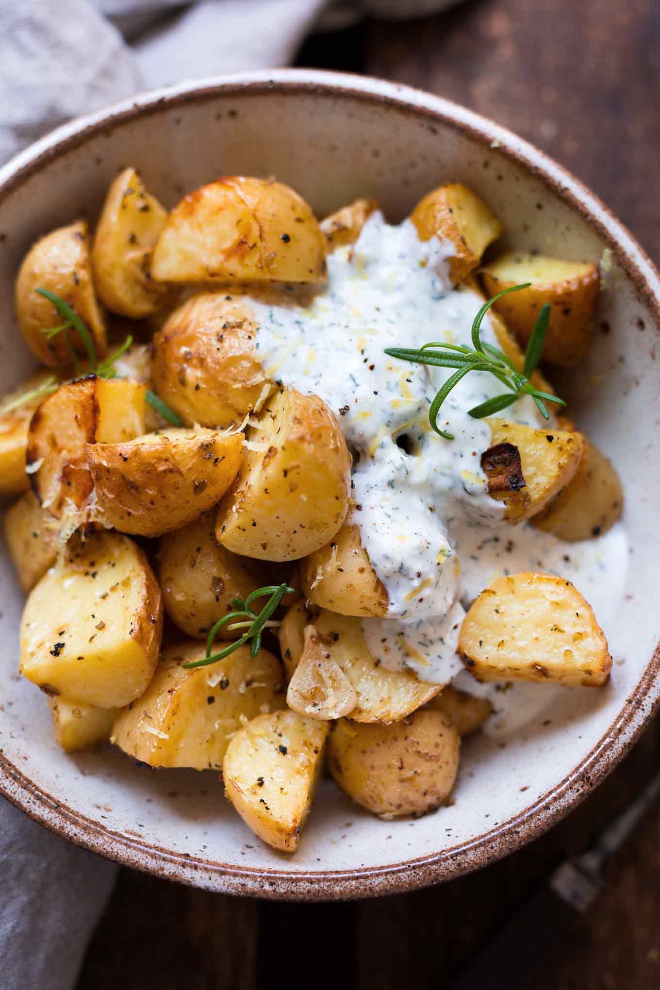 Griechische Ofenkartoffeln mit Joghurt-Feta-Dip in einer Schüssel auf einem braunen Holzuntergrund. Getoppt mit frischem Rosmarin.