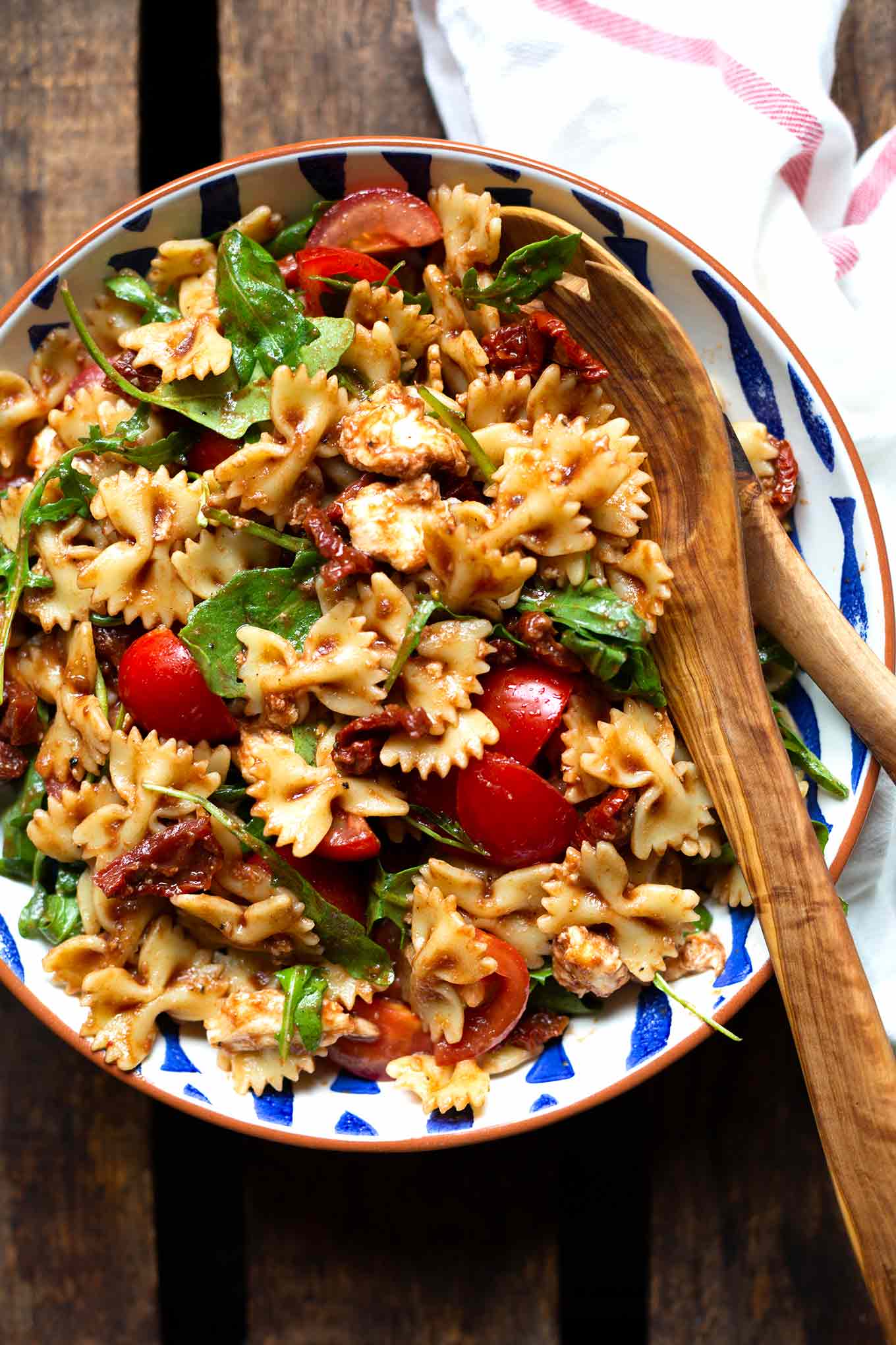 Italienischer Nudelsalat in einer Schüssel mit zwei Holzlöffeln zum Servieren.