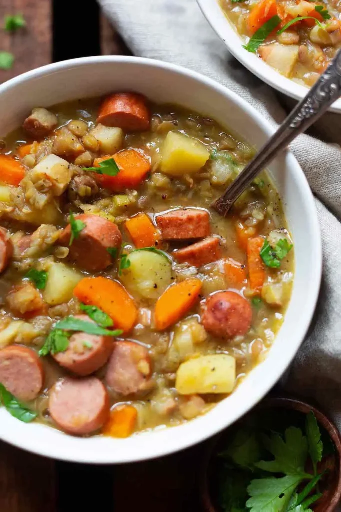 Omas Linsensuppe mit Würstchen, Karotten und Kartoffeln in einer Schüssel.