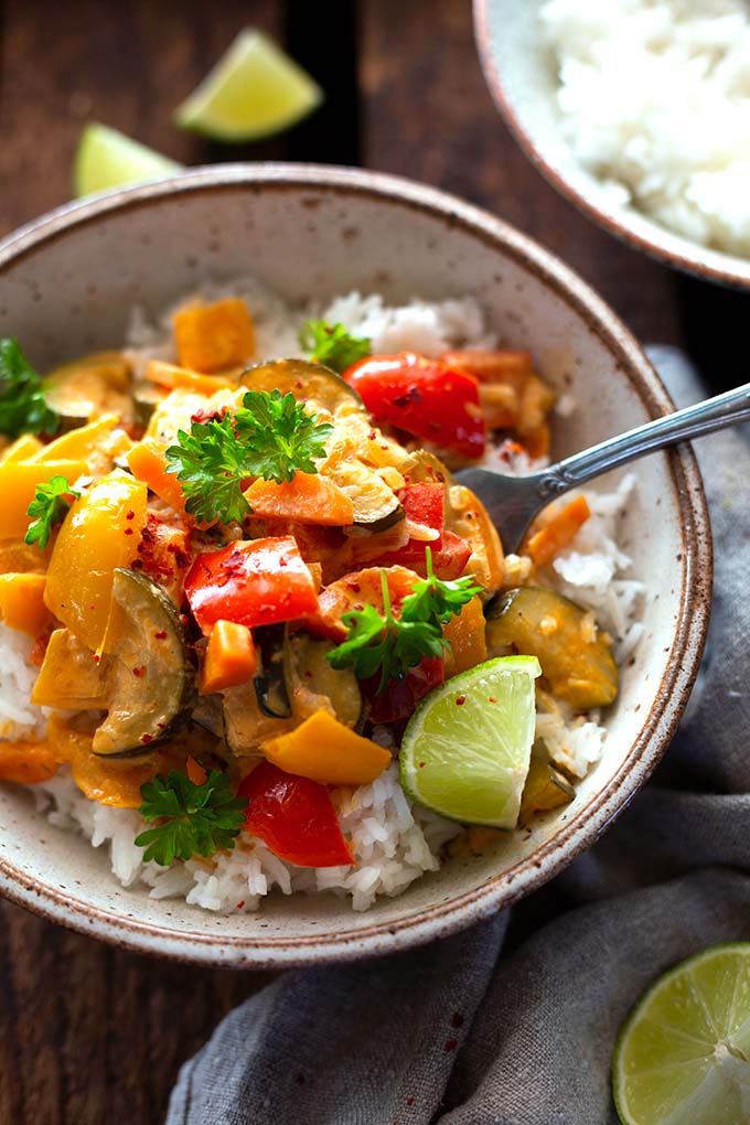 Thai-Gemüse-Curry mit Kokosmilch & roter Currypaste in einer Schüssel mit Reis. Serviert mit Limetten.