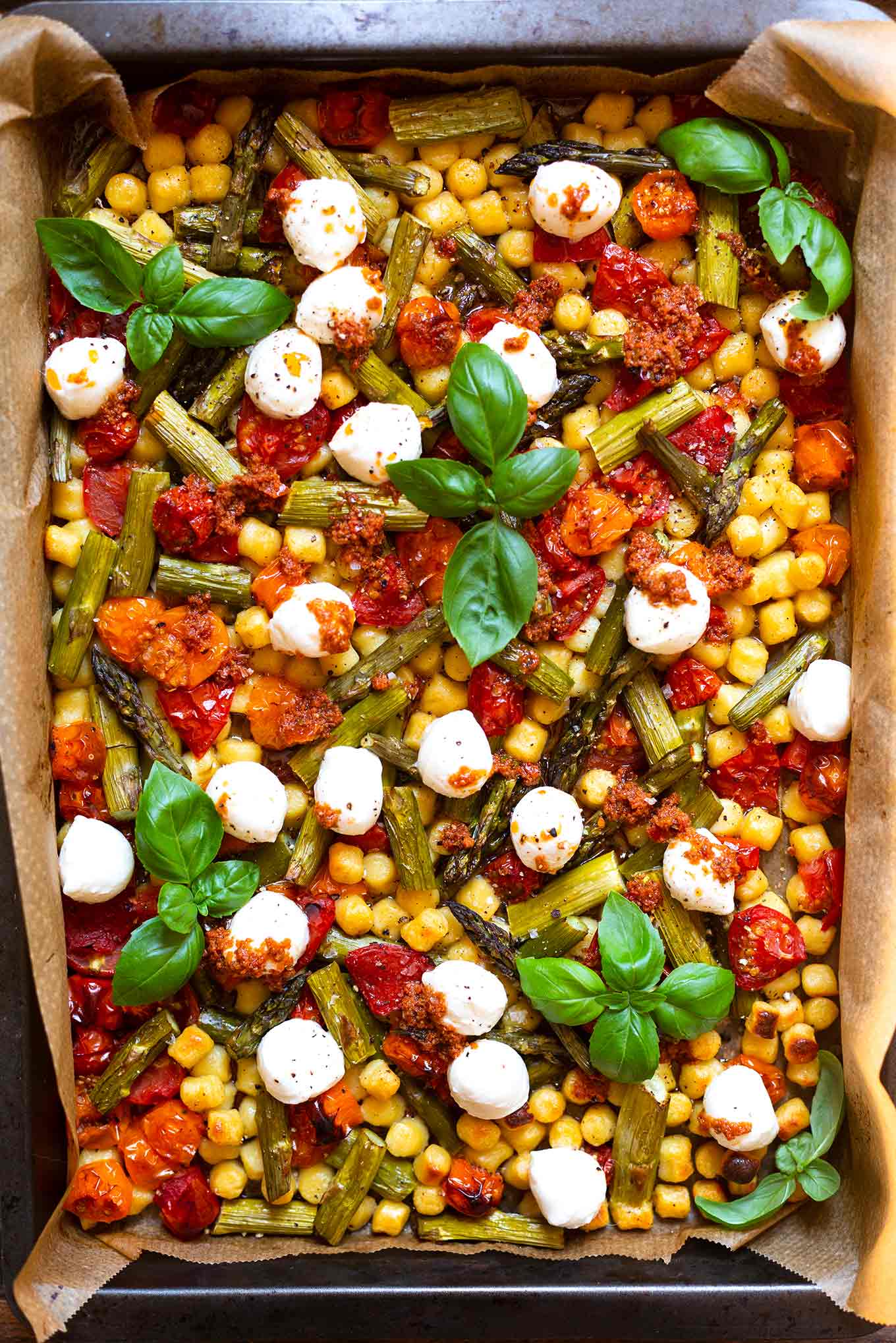Ein Blech vollgepackt mit Gnocchi, grünem Spargel, Tomaten und Mozzarella