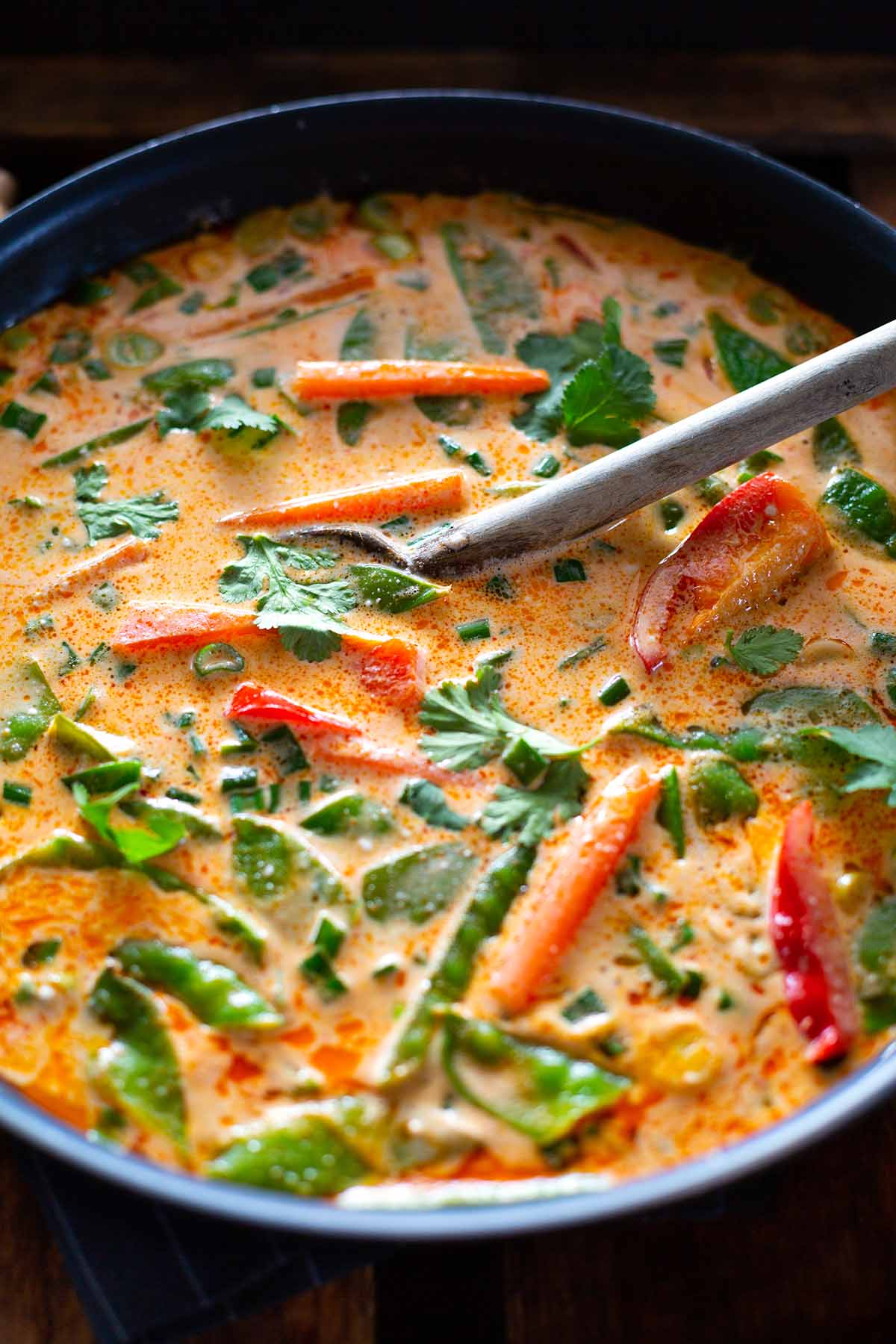 Veganes rotes Thai-Curry mit Kokosmilch während der Zubereitung in einer großen Pfanne.