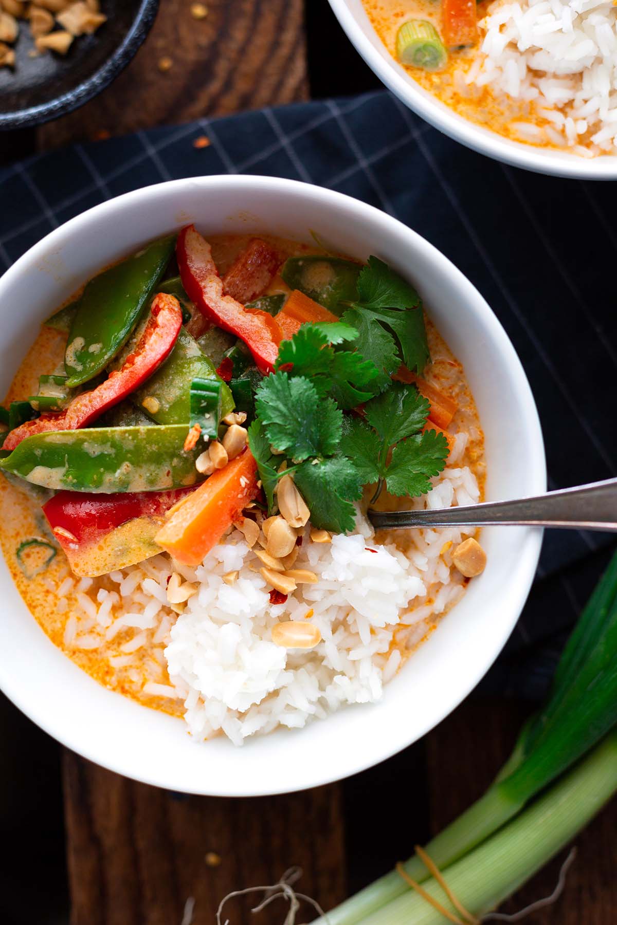 Veganes rotesThai-Curry mit Kokosmilch in einer weißen Schüssel mit Reis und Nüssen angerichtet, mit Koriander dekoriert.