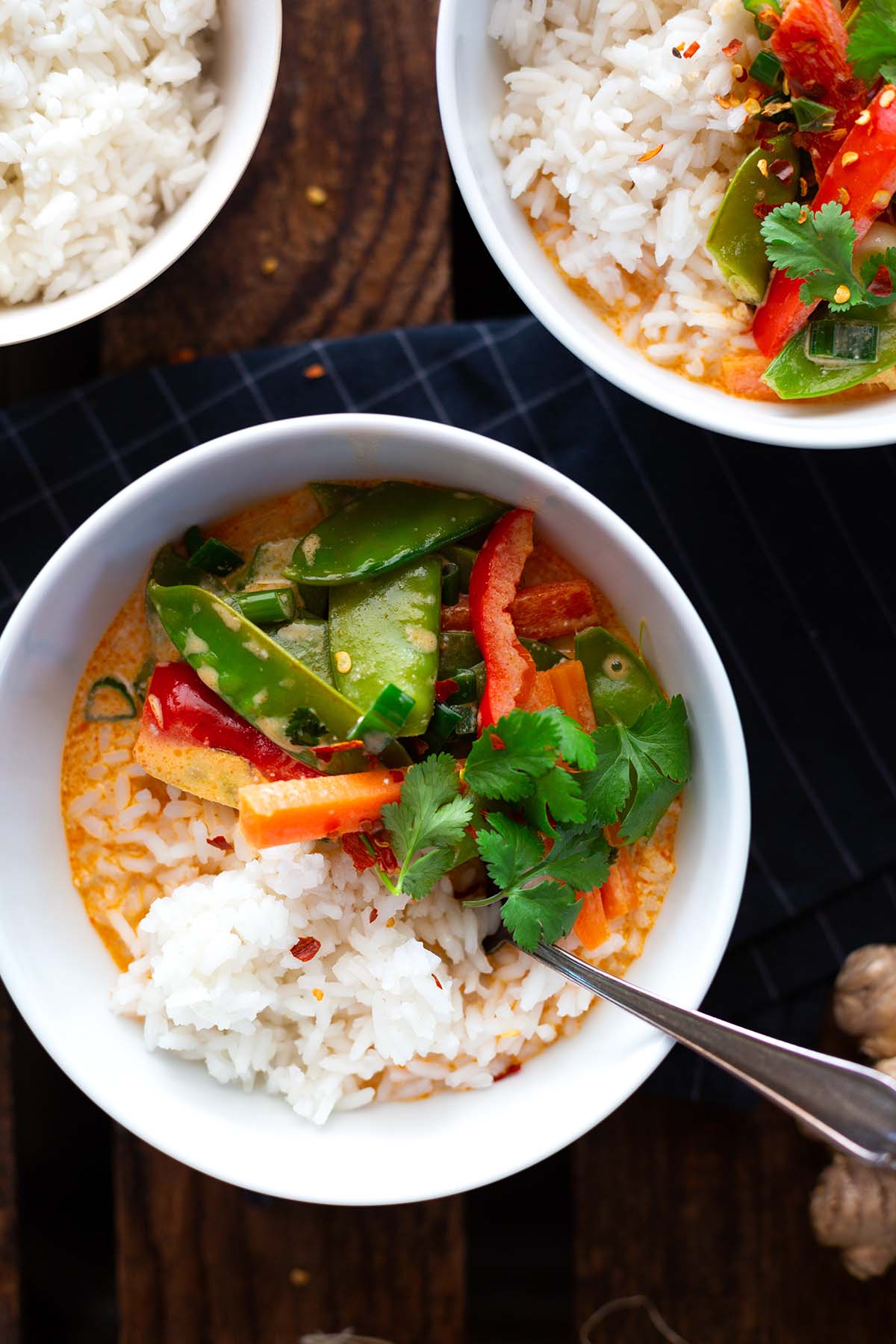 Veganes rotes Thai-Curry mit Kokosmilch in einer weißen Schüssel mit Reis und Nüssen angerichtet, mit Koriander dekoriert.