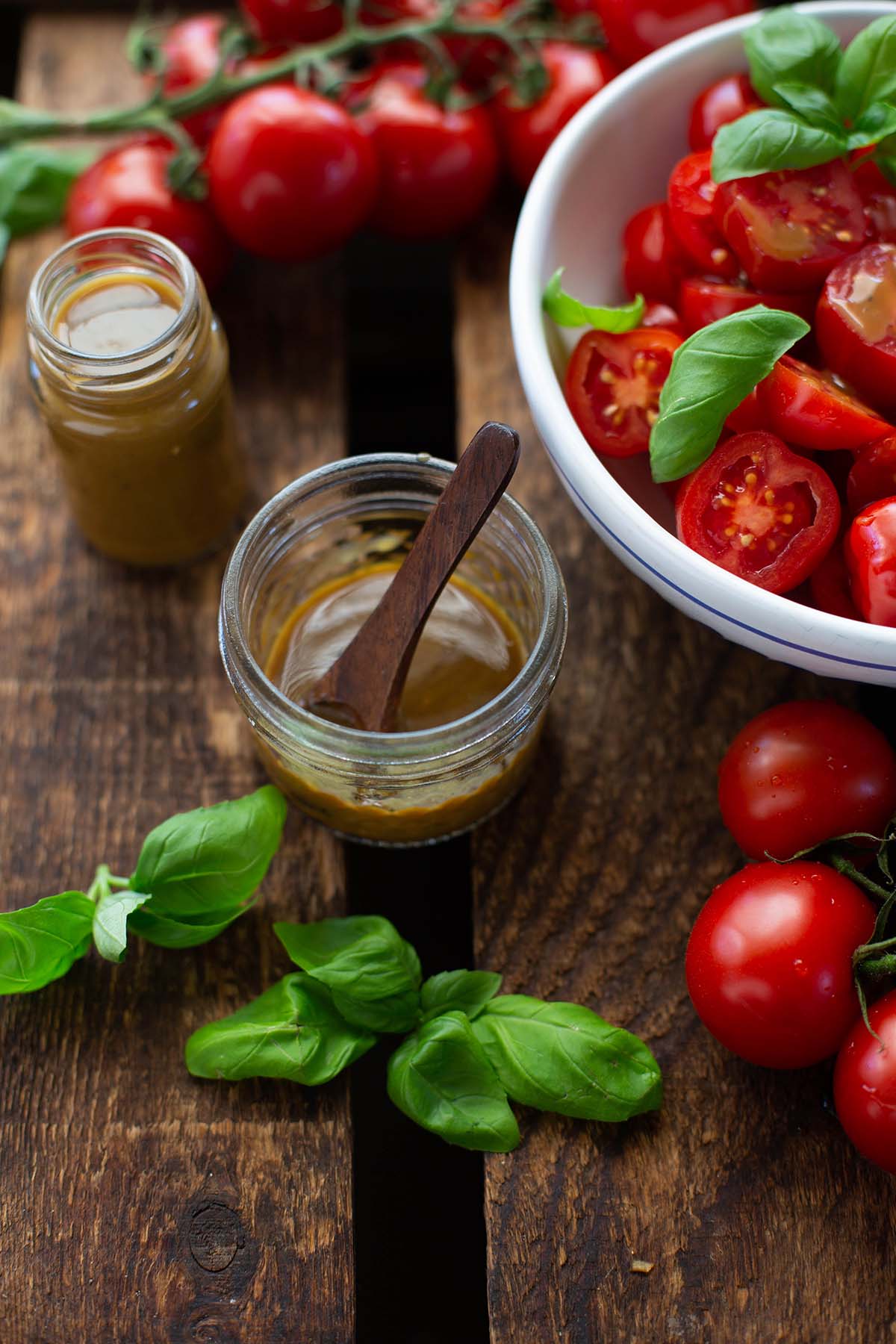 Schnelles Balsamico-Dressing in einem Marmeladenglas mit einem Löffel angerichtet mit frischen Tomaten und Basilikum.