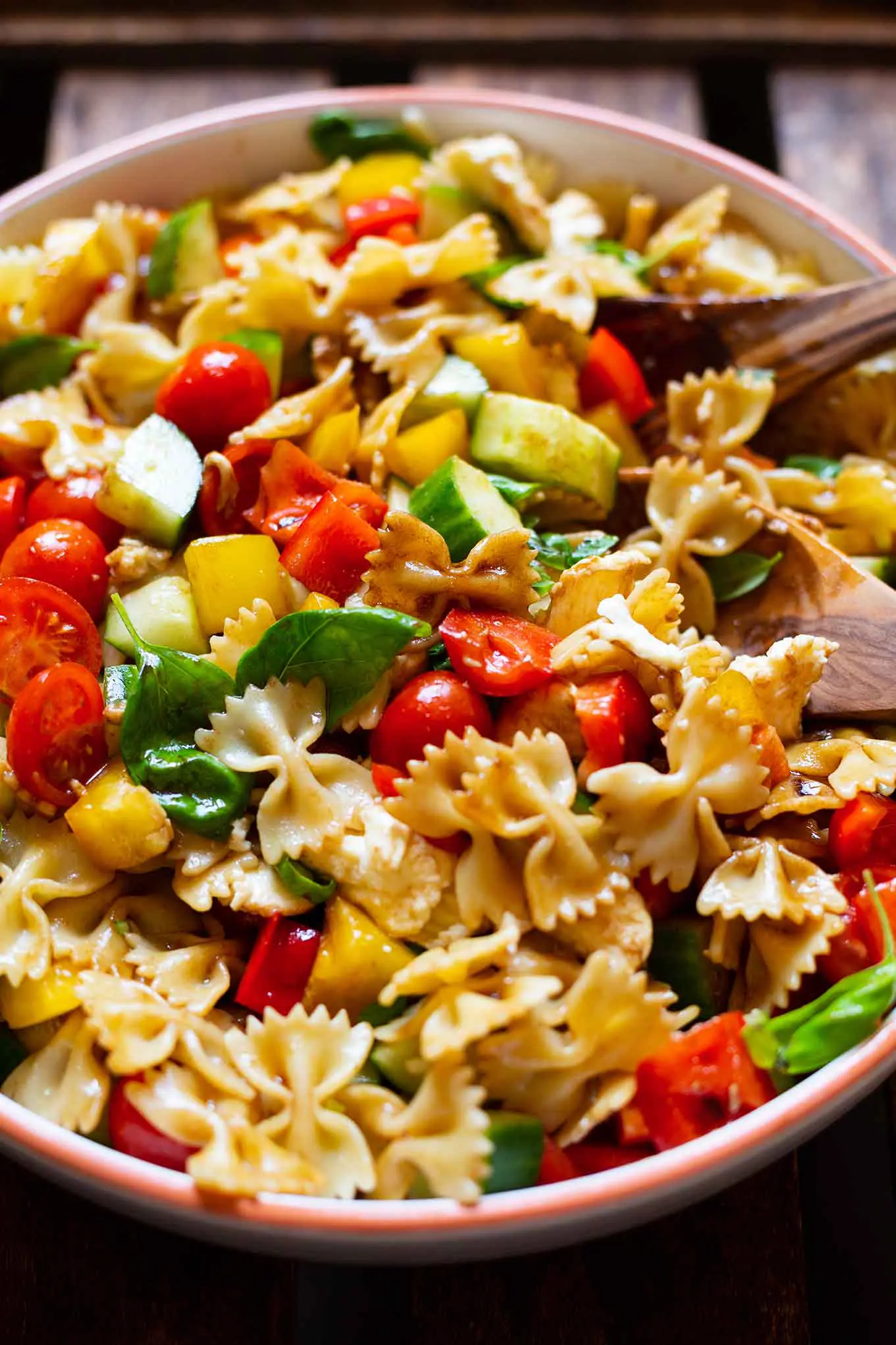 Bunter Nudelsalat in einer großen Steingut Schüssel mit Olivenholz-Löffeln zum Auffüllen.