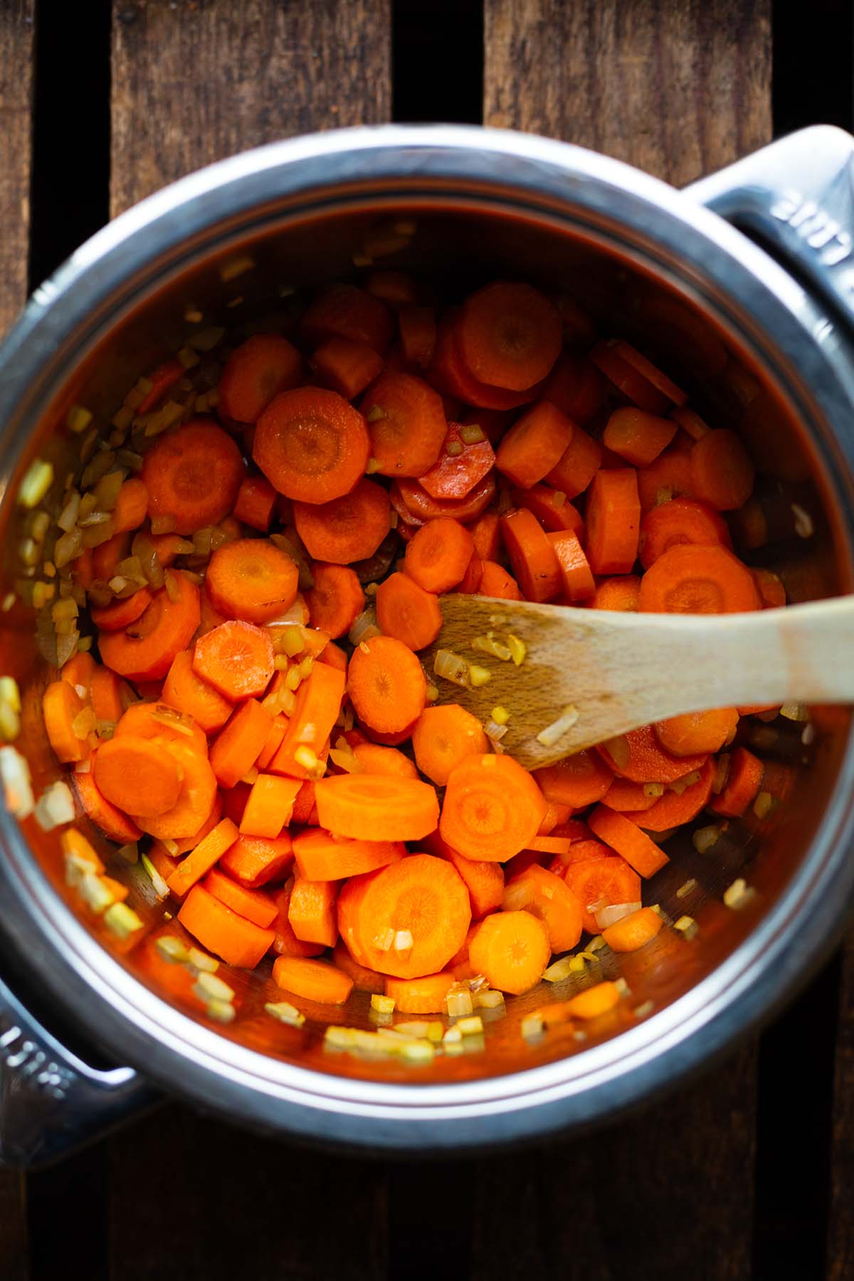 Kleingeschnittene Möhren für die Möhrensuppe mit Ingwer und Kokosmilch werden zusammen mit Zwiebeln in einem Topf angebraten.