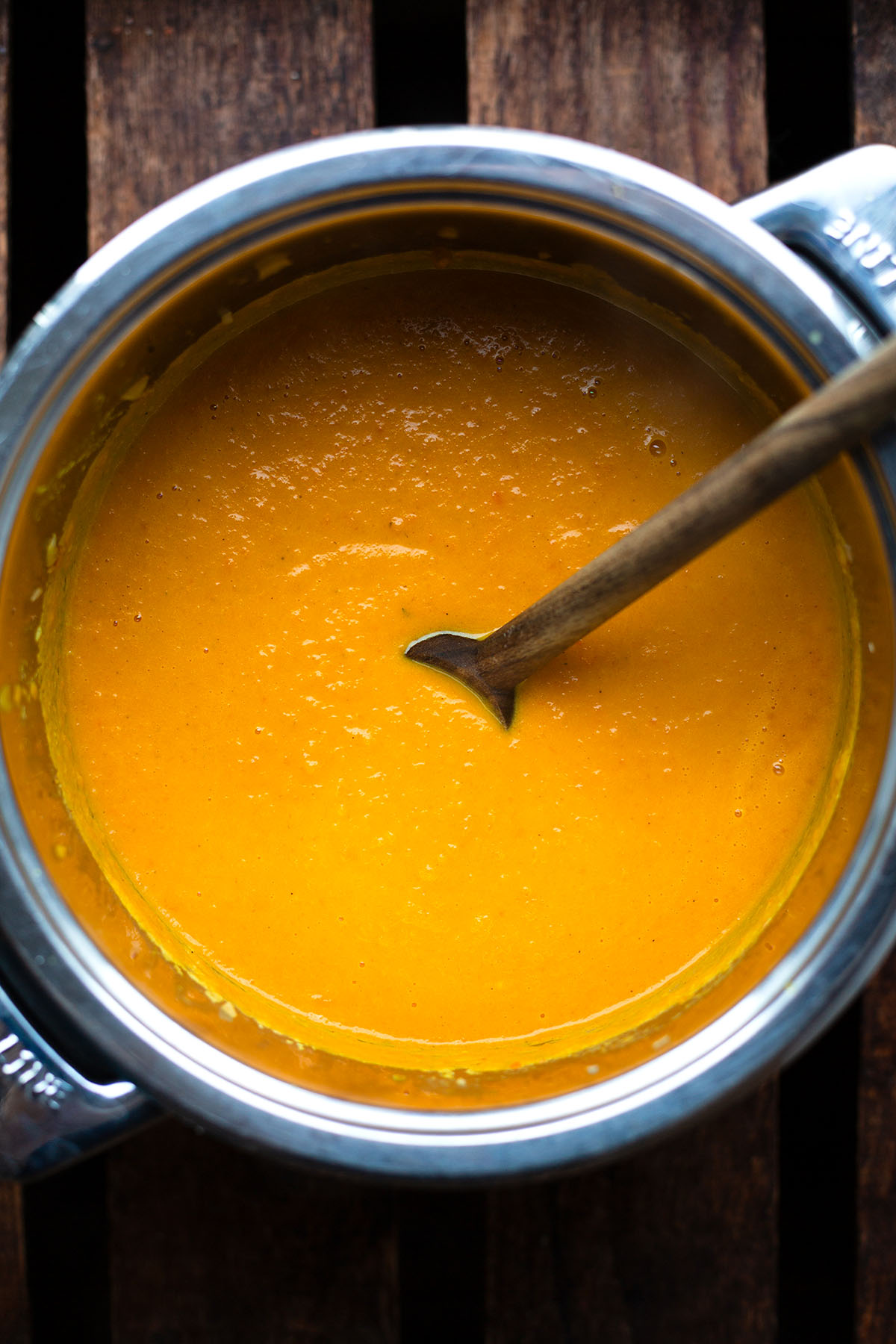 Fertige pürierte vegane Möhrensuppe in einem Topf wird mit einem Holzlöffel umgerührt.