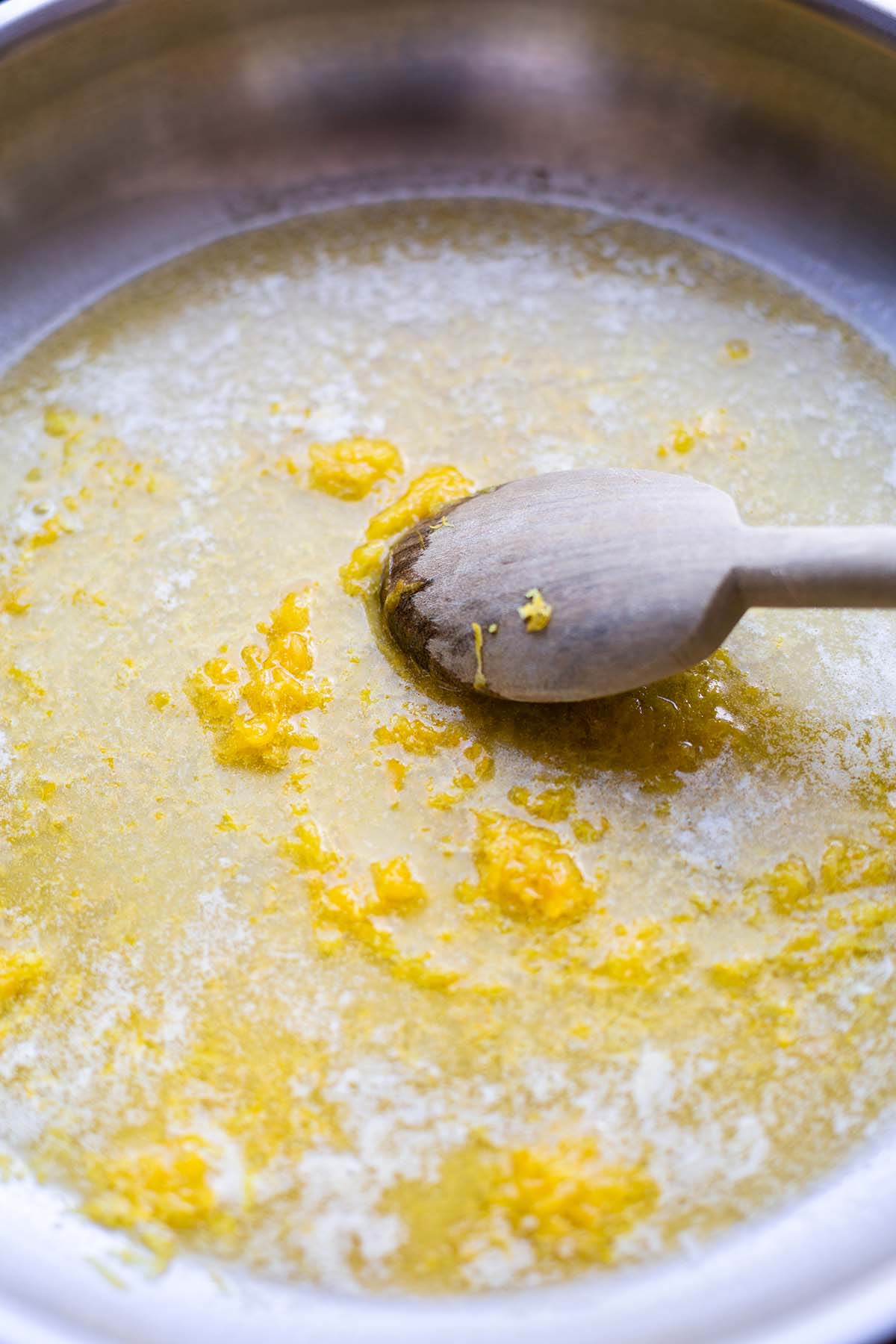 Geschmolzene Butter mit Zitronenabrieb wird in einer Pfanne mit einem Holzlöffel umgerührt.