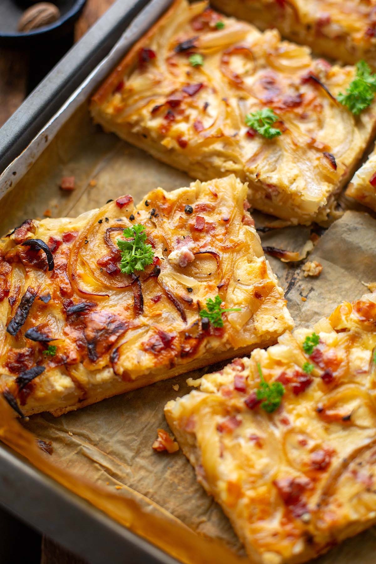 Zwiebelkuchen auf einem Blech, in Stücke geschnitten und mit Petersilie getoppt