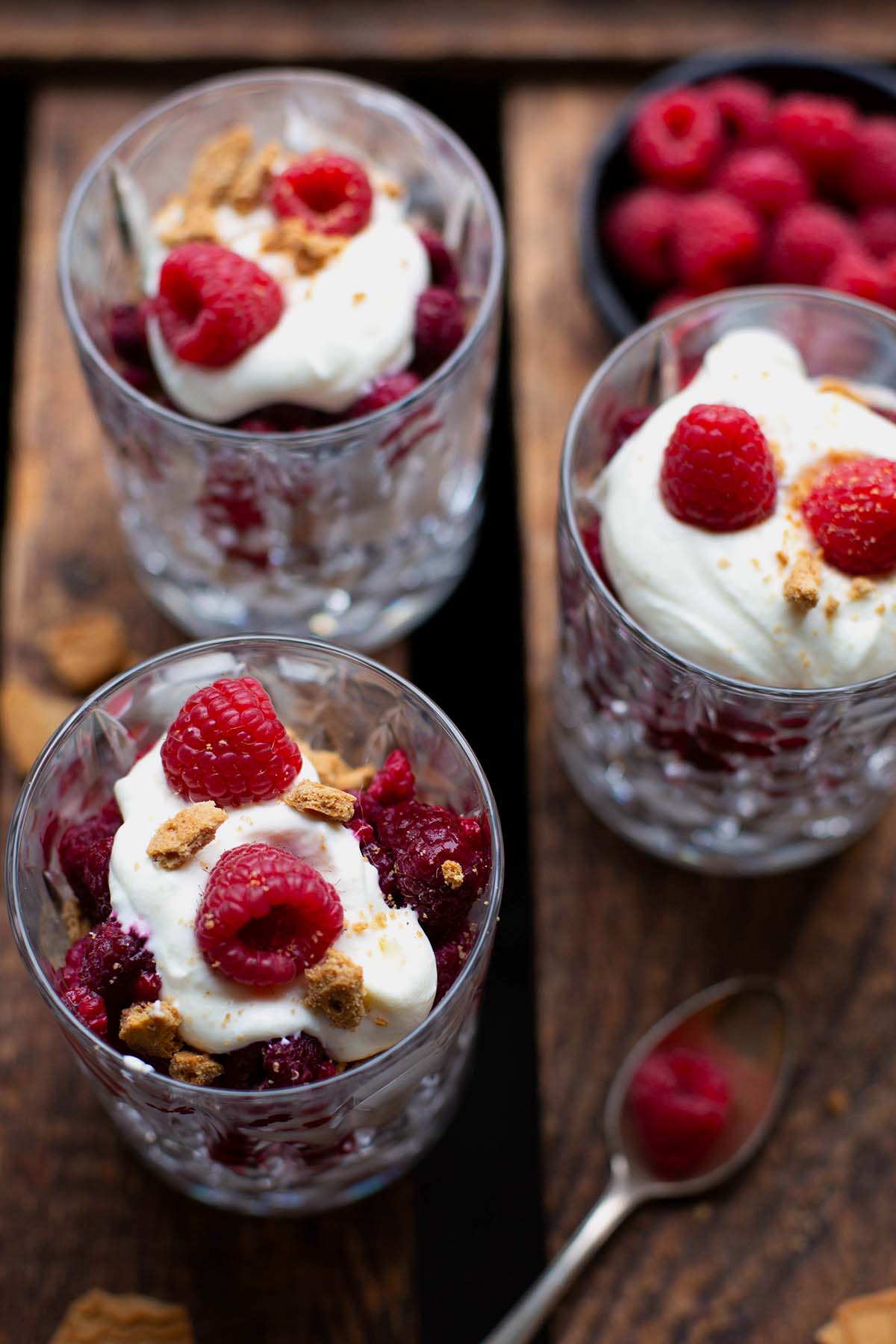 Fertiges Spekulatius-Tiramisu mit gefrorenen Himbeeren auf dunklem Holzuntergrund, aufgeteilt auf drei Gläser.