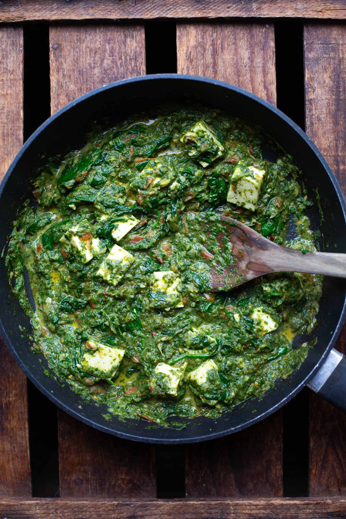 Palak Paneer mit Spinat, indischem Frischkäse und Gewürzen in einer Pfanne auf einem dunklen Untergrund.