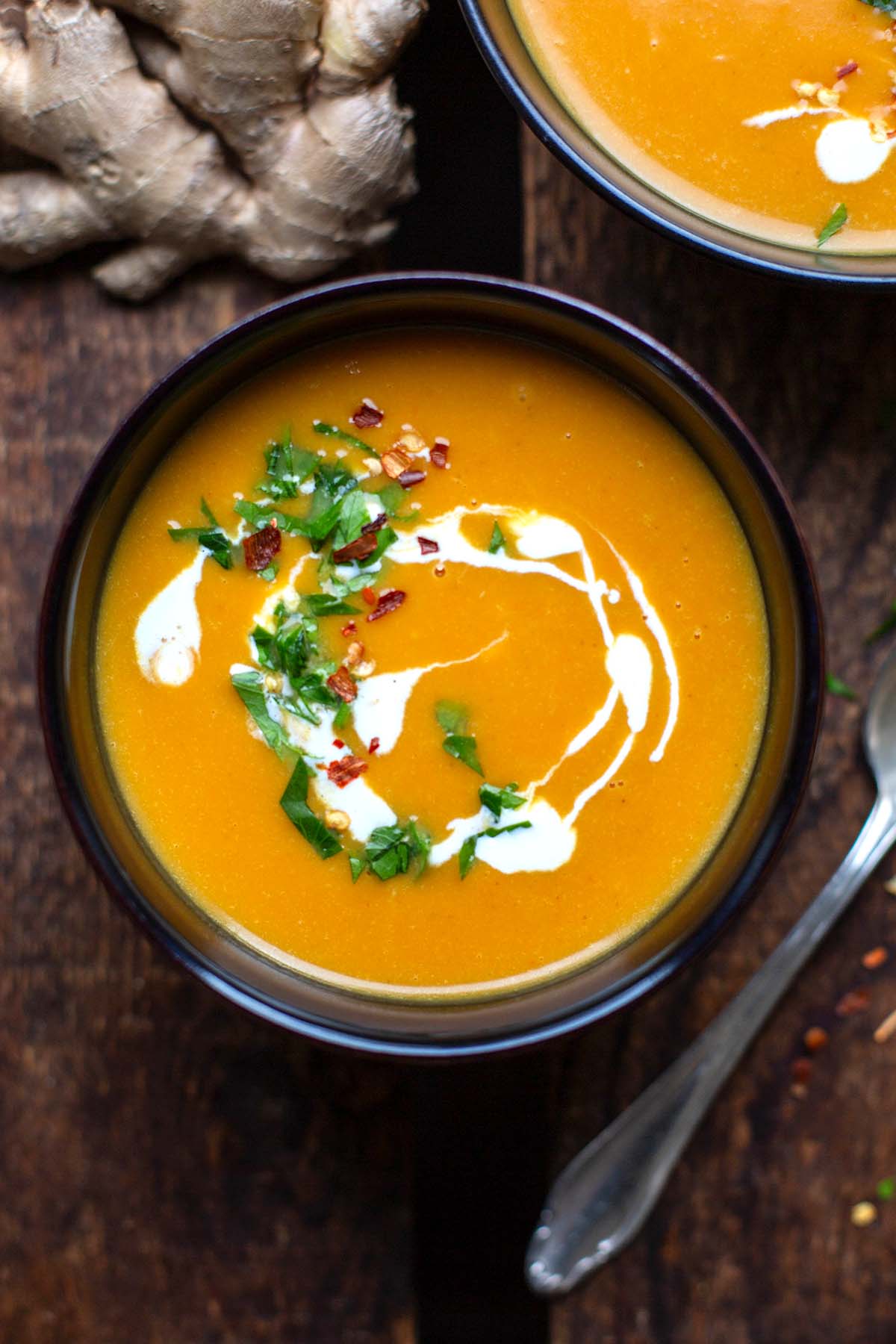 Süßkartoffelsuppe mit Kokosmilch und Ingwer in einer schwarzen Schüssel. Getoppt mit Chiliflocken und Petersilie