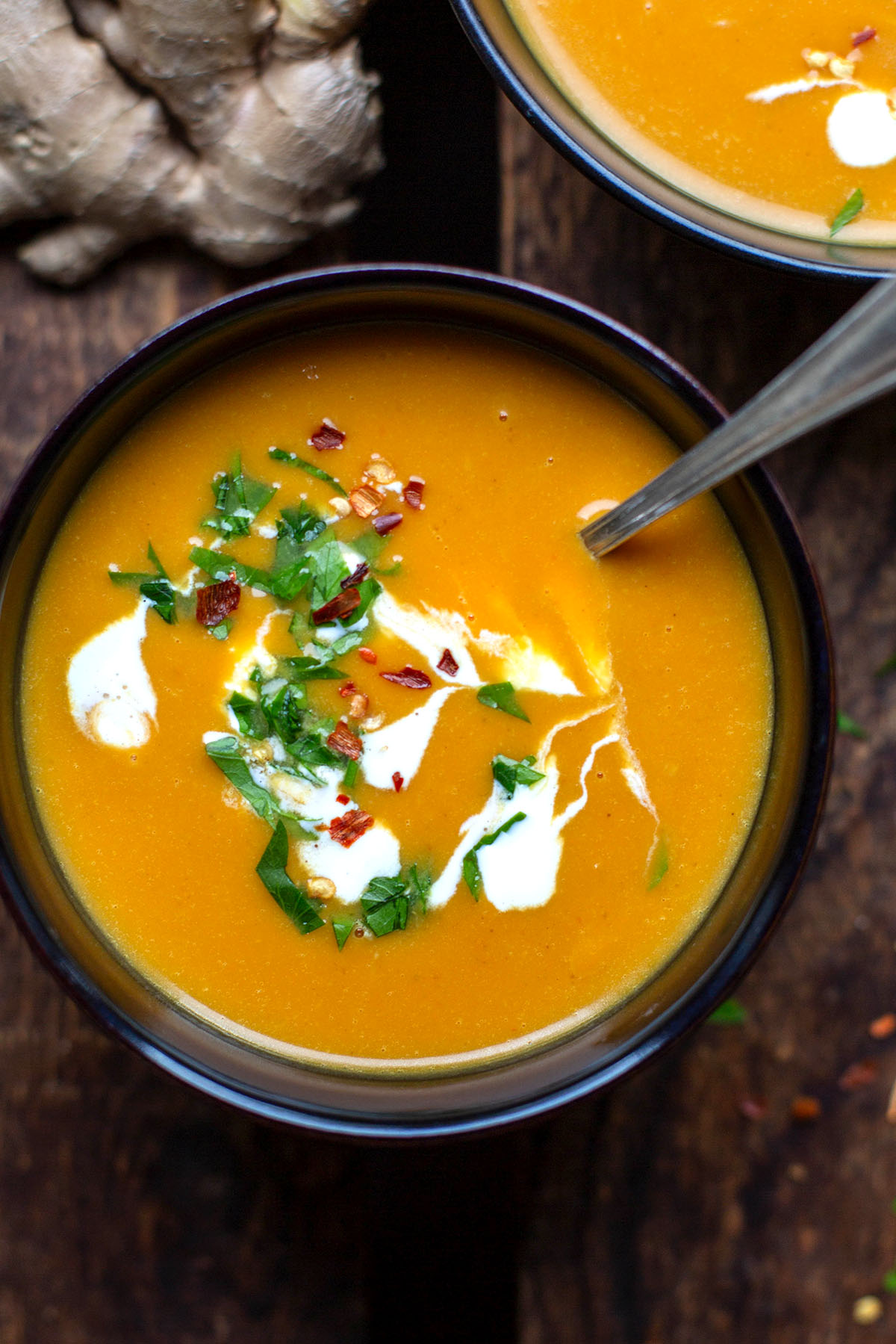 Süßkartoffelsuppe mit Kokosmilch und Ingwer in einer schwarzen Schüssel. Getoppt mit Chiliflocken und Petersilie