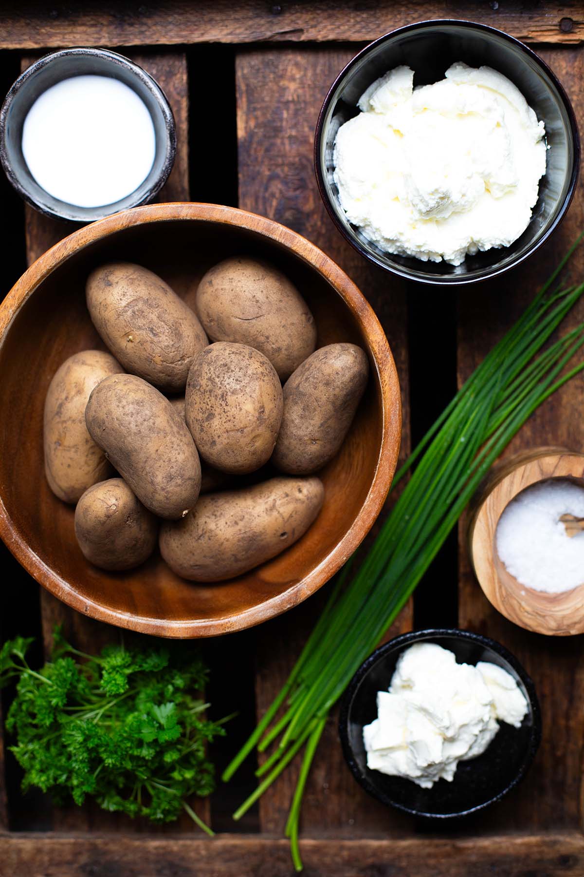 Zutaten für die Pellkartoffeln mit Quark in einzelnen Schüsseln. Zu sehen sind Milch, Quark, Kartoffeln, Schmand, Schnittlauch, Petersilie.