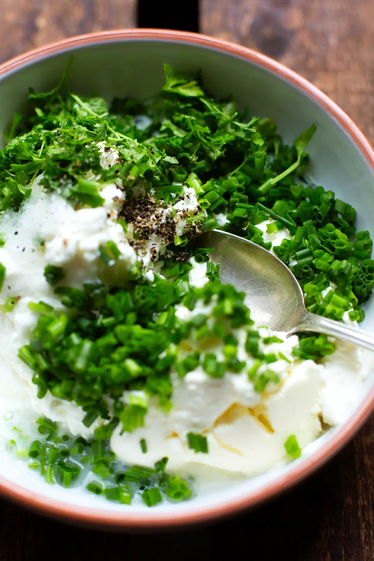 Die Zutaten für das Kräuterquark Rezept in einer Schüssel vor dem Verrühren. Zu sehen sind Schnittlauch, Magerquark, Zitronensaft, Schmand, Salz und Pfeffer.