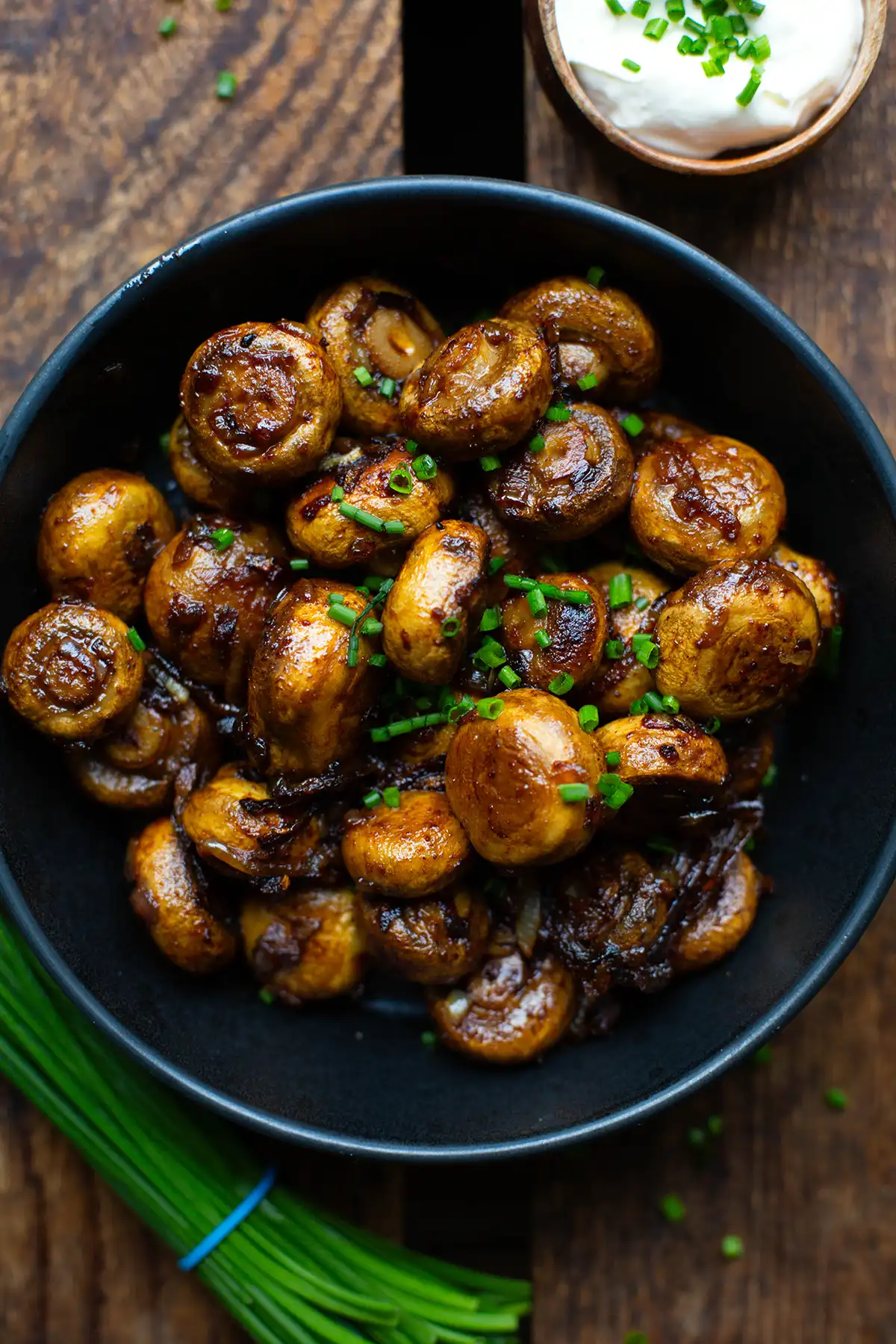 Champignons wie vom Weihnachtsmarkt angerichtet in einer schwarzen Schüssel mit Knoblauch-Dip in einer kleinen Holzschüssel und frischem Schnittlauch auf einem dunklen Holzuntergrund.