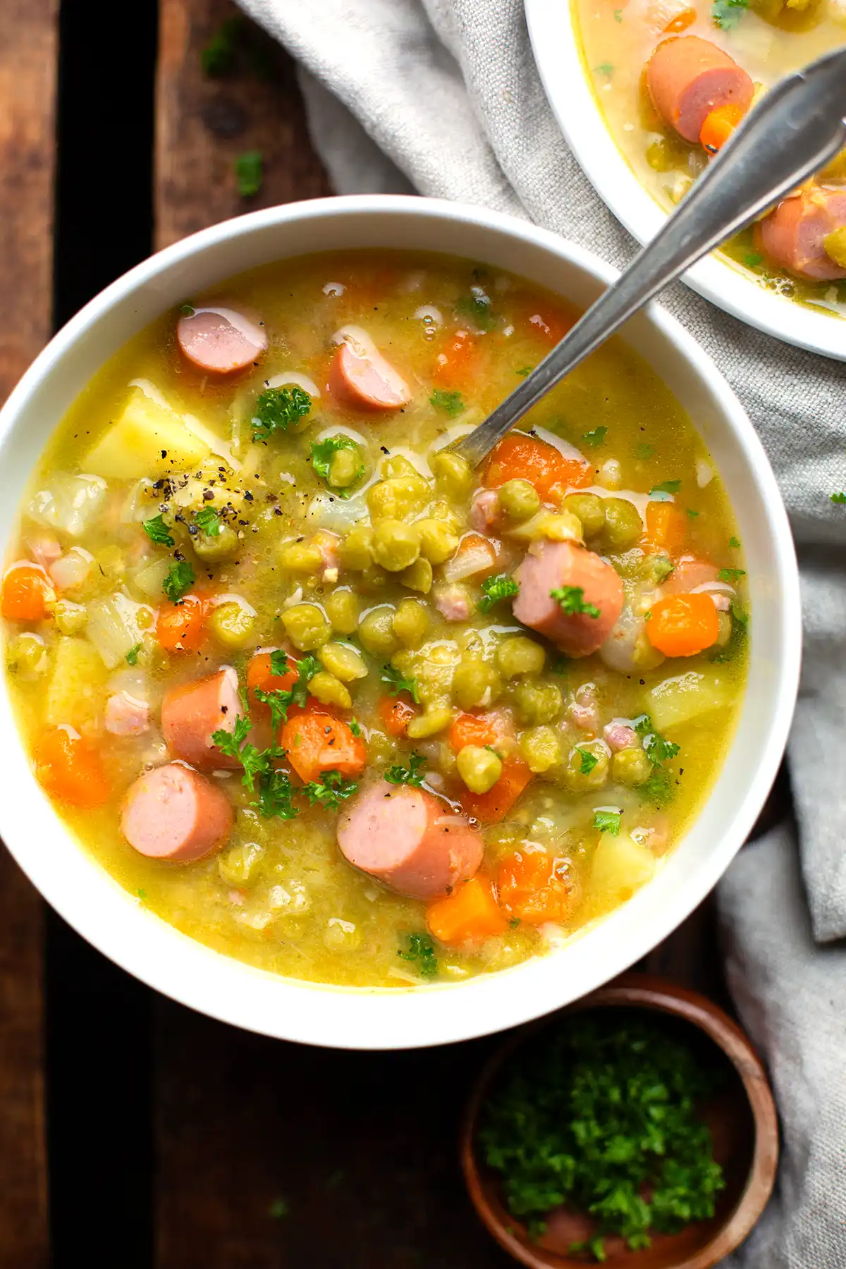 Erbsensuppe mit Würstchen, Kartoffeln und Gemüse in einer weißen Schüssel. Getoppt mit Petersilie