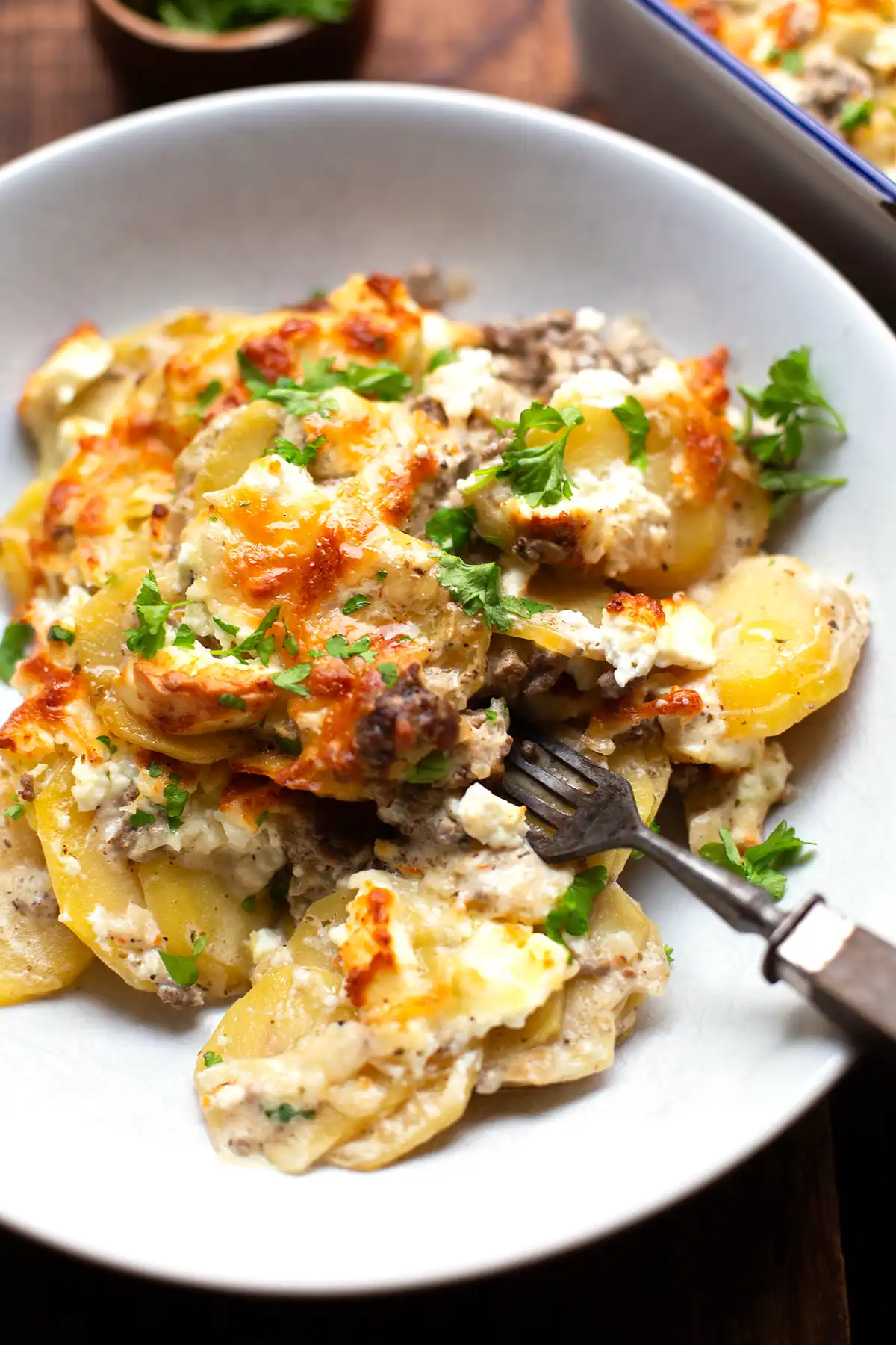 Kartoffel-Hackfleisch-Auflauf angerichtet auf einem weißen Teller als einzelne Portion mit Petersilie bestreut.