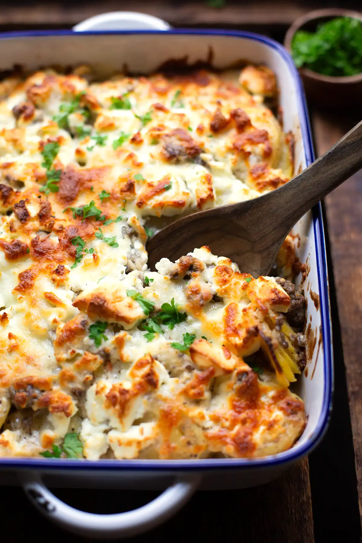 Kartoffel-Hackfleisch-Auflauf mit Käse überbacken in einer Auflaufform und einem Holzlöffel zum Auffüllen.