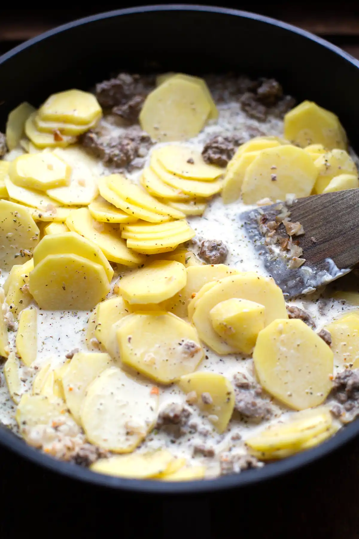 Der Auflauf in Zubereitung. Zu sehen sind angebratenes Hackfleisch, Kartoffeln, Zwiebeln und Gewürze gemischt in einer großen Pfanne.