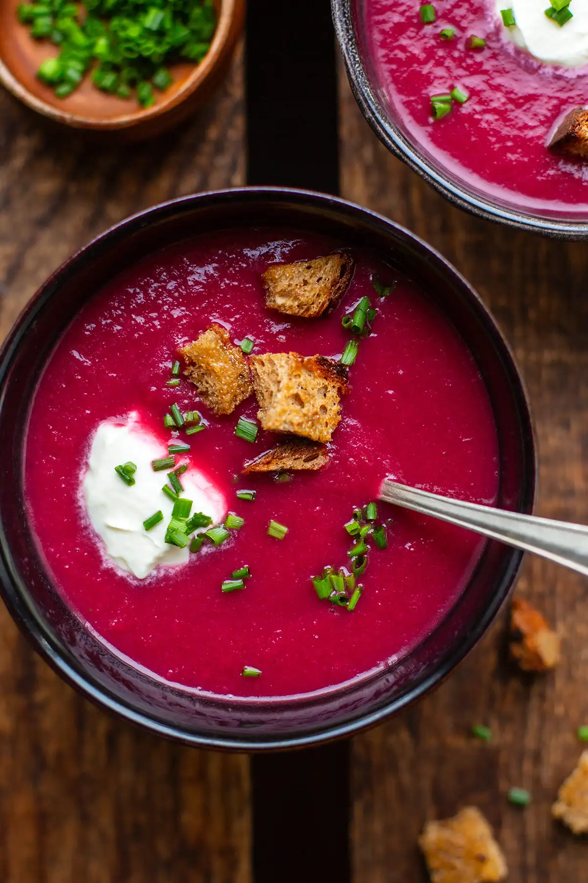 Fertige, pürierte Rote-Bete-Suppe in einer dunklen Schüssel, garniert mit Croutons, Schmand und Schnittlauch