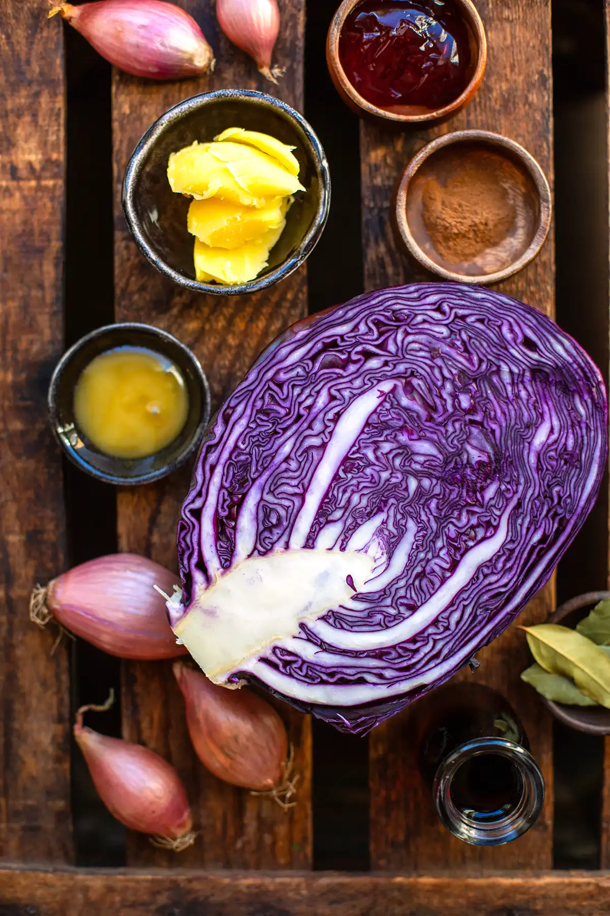 Zutaten für klassisches Rotkohl Rezept: Rotkohl, Honig, Johannisbeergelee, Gewürze, Schalotten und Rotwein auf einer Arbeitsfläche.