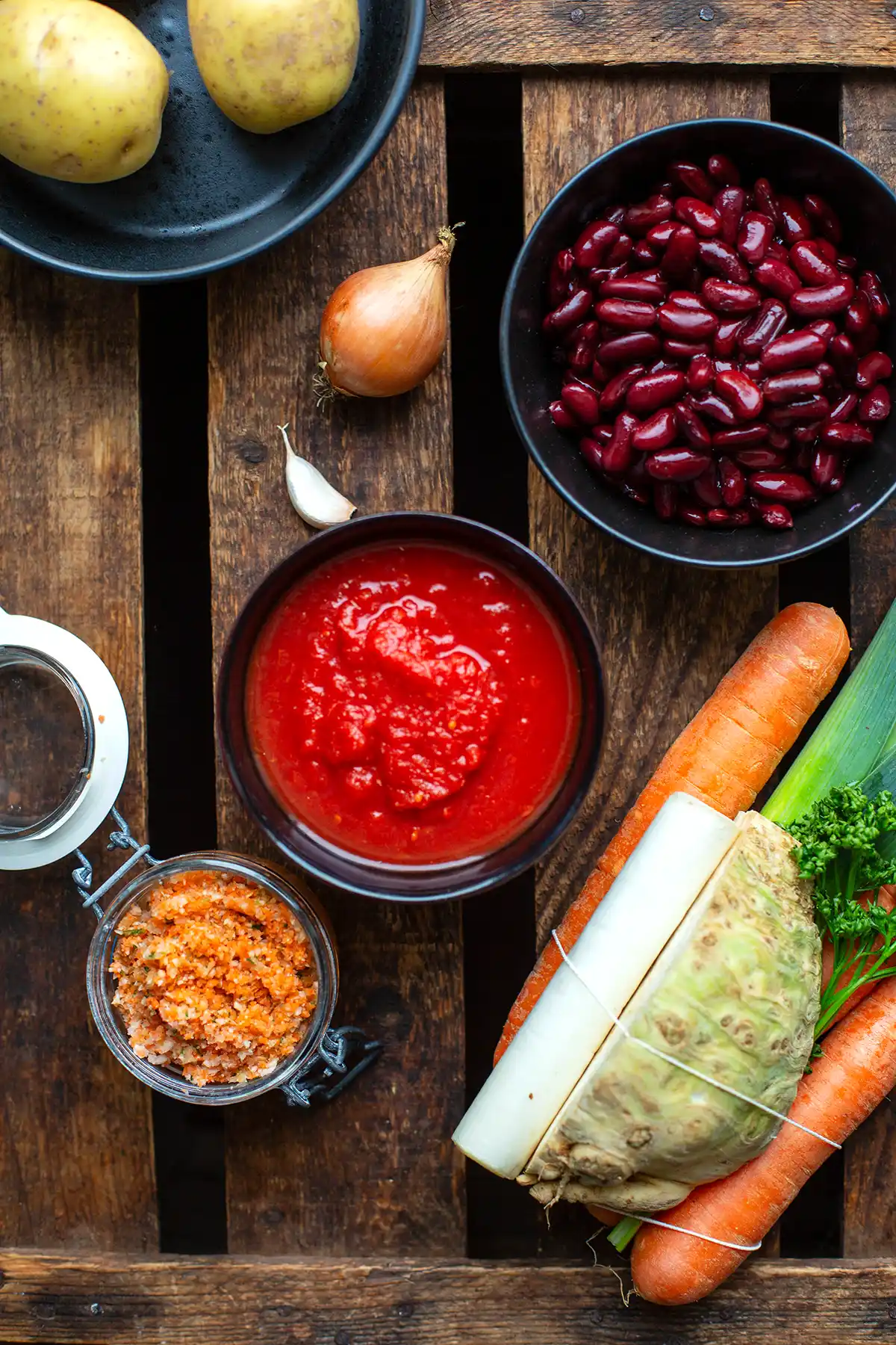 Die Zutaten für den deftigen Gemüseeintopf: Suppengrün, Bohnen, gehackte Tomaten, Gemüsebrühe, Zwiebel, Knoblauch und Kartoffeln