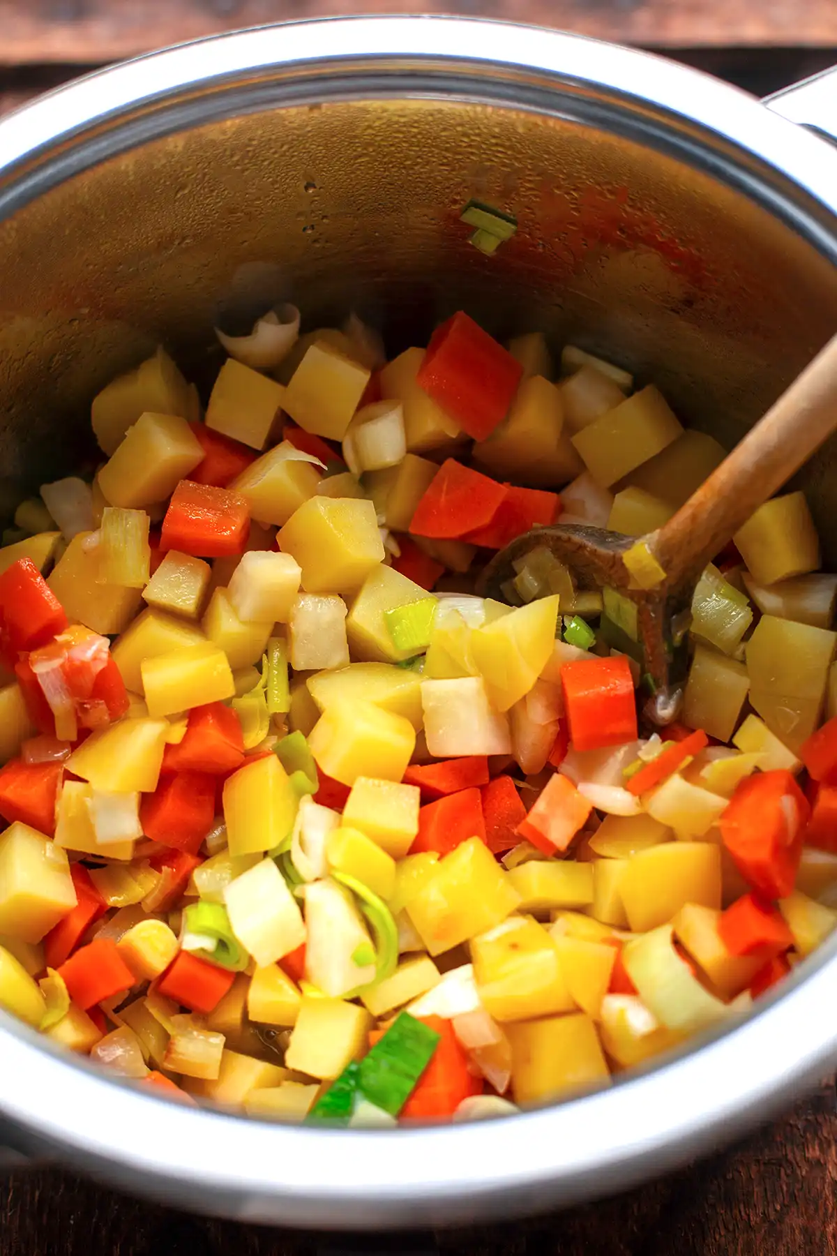 Frisches Suppengemüse und Kartoffelwürfel werden in einem großen Topf für den vegetarischen Gemüseeintopf angebraten.