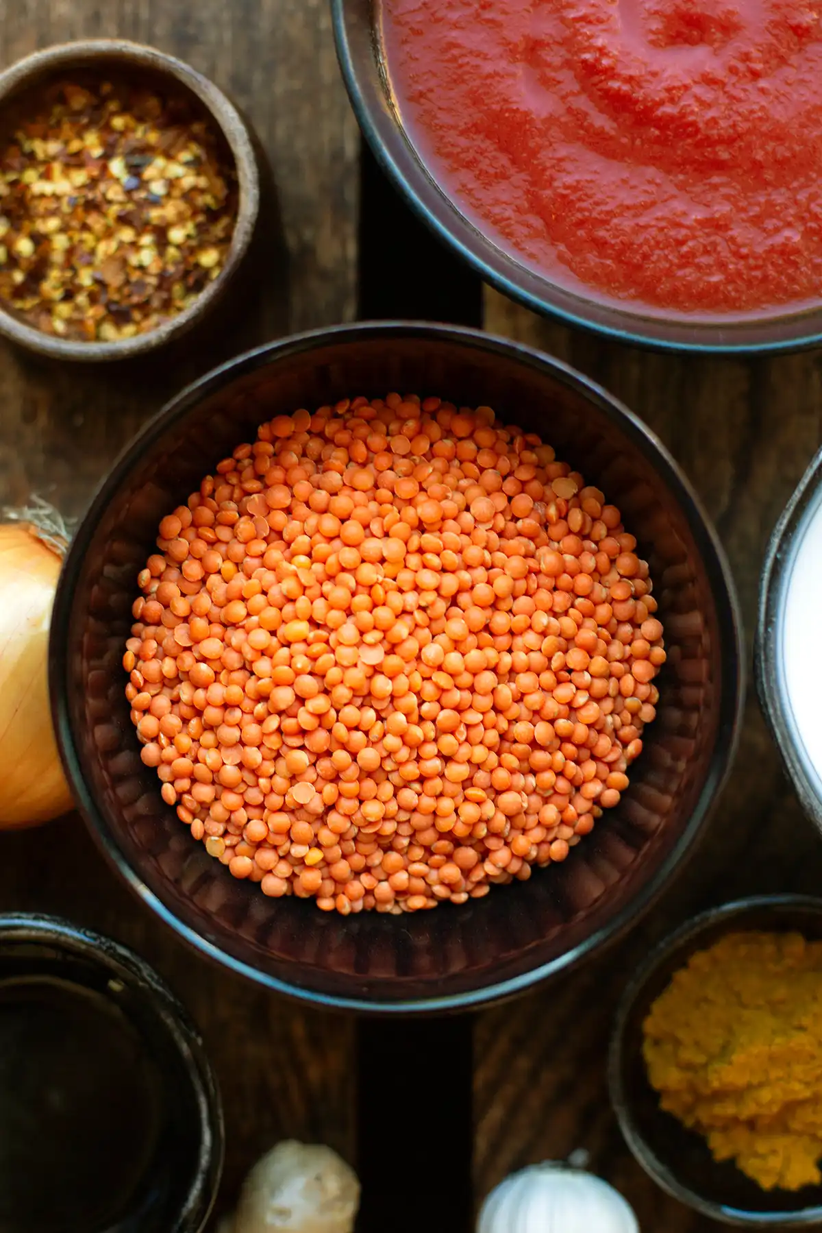 Zutaten für indisches Dal: rote Linsen, Kokosmilch, Kurkuma, Ingwer, Zwiebel und Knoblauch auf einem Holzuntergrund.