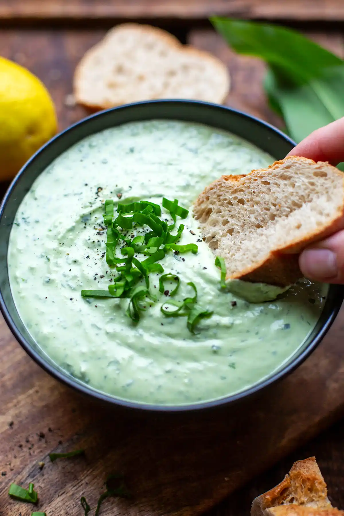 Bärlauch-Dip mit Feta und Frischkäse in einer Schüssel. in den ein Stück Baguette gedippt wird.