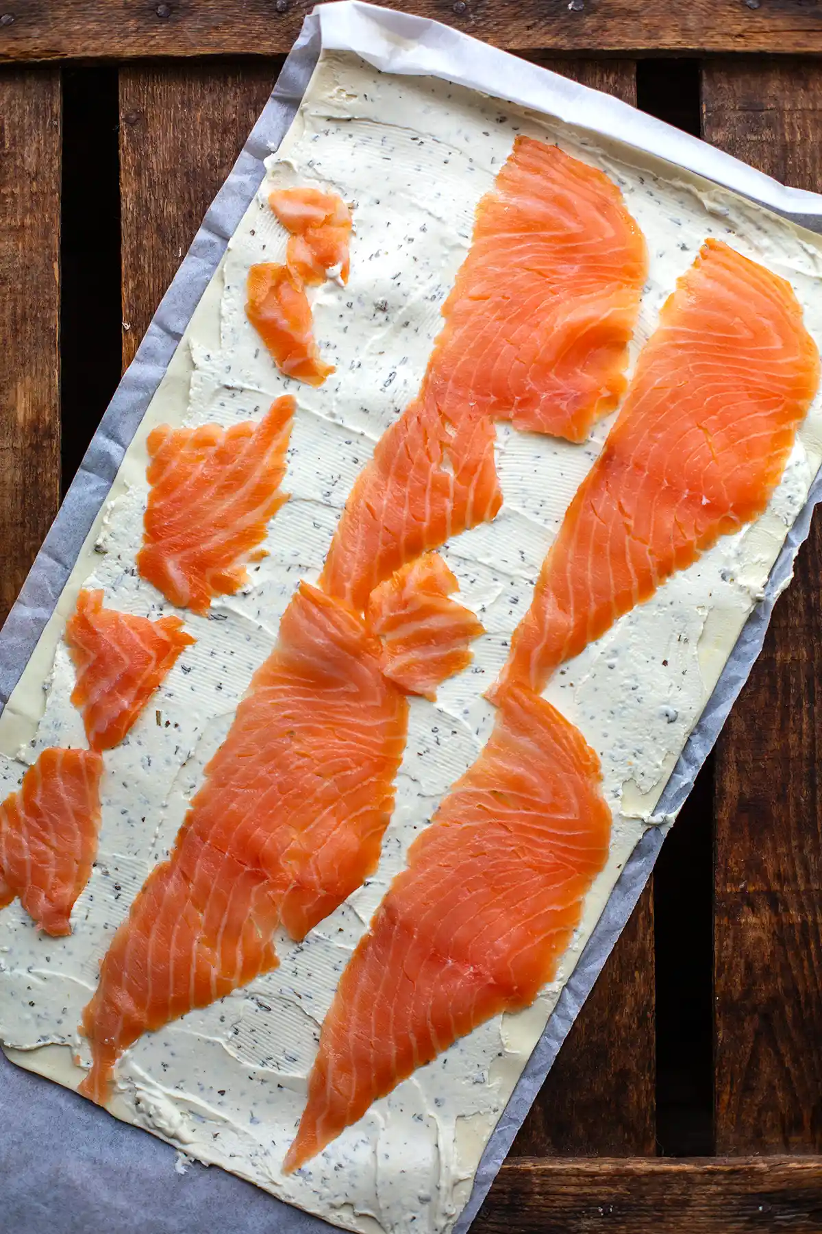 Blätterteig wird mit Kräuterfrischkäse bestrichen und mit Räucherlachs belegt für einfache Lachs-Schnecken.