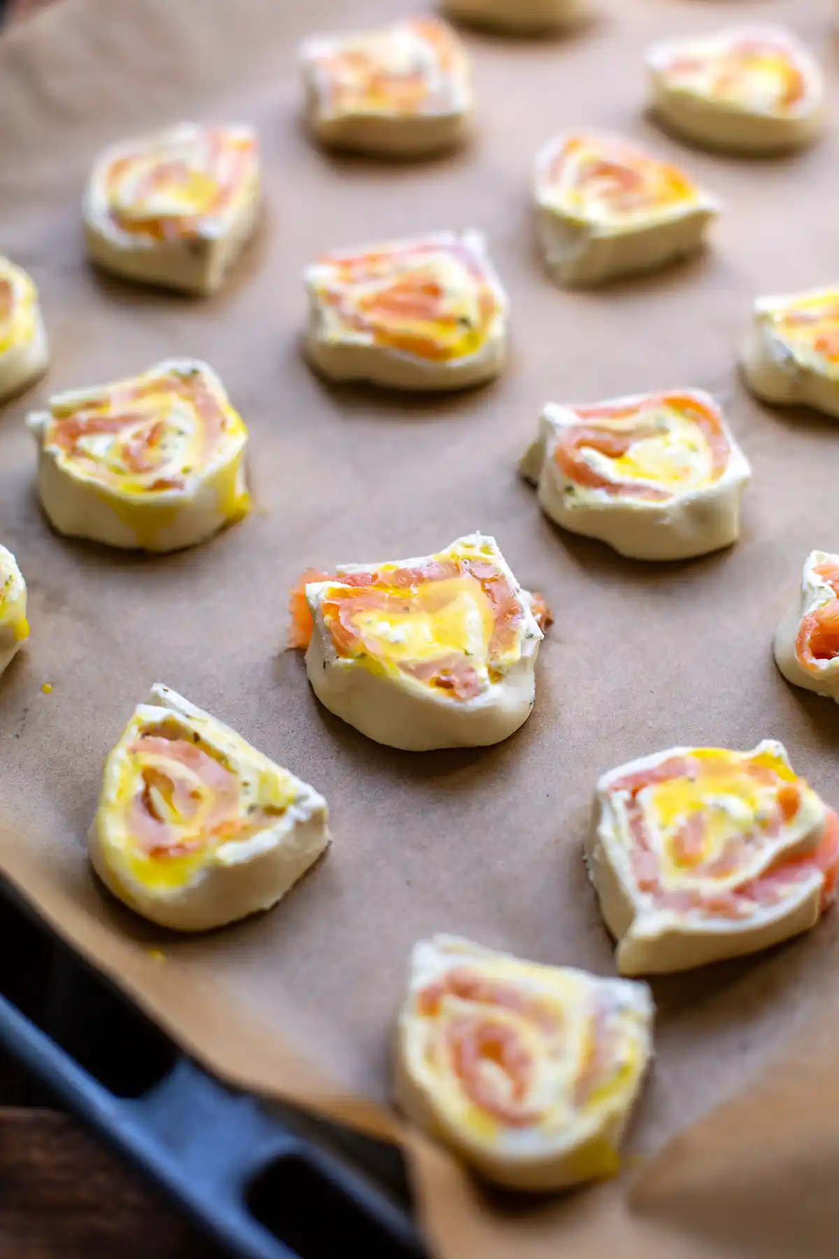 Rohe Blätterteigschnecken mit Lachs liegen auf einem mit Backpapier belegten Backblech, bereit für den Ofen.