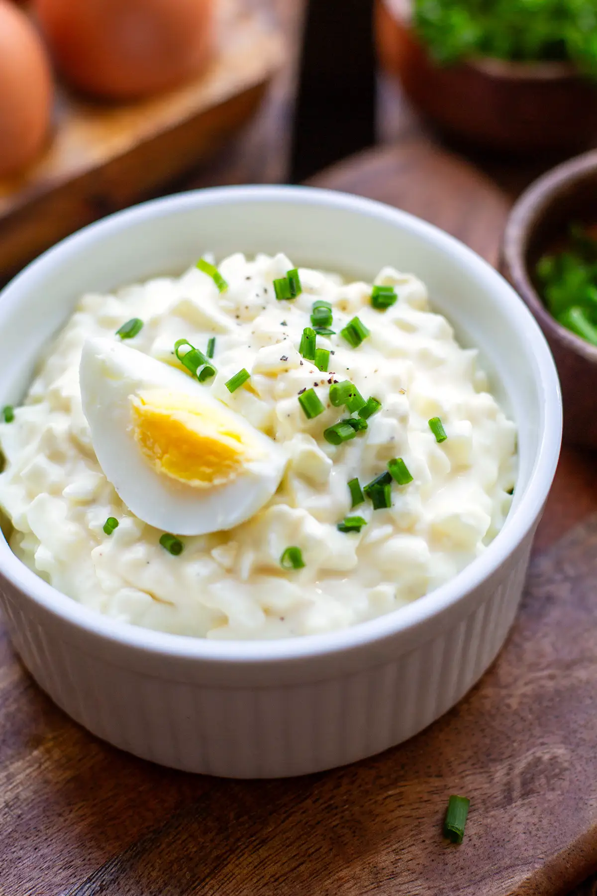Klassischer Eiersalat wie von Oma angerichtet in einer weißen Schüssel bestreut mit Schnittlauch und Pfeffer, Garniert mit einem hart gekochten Ei.
