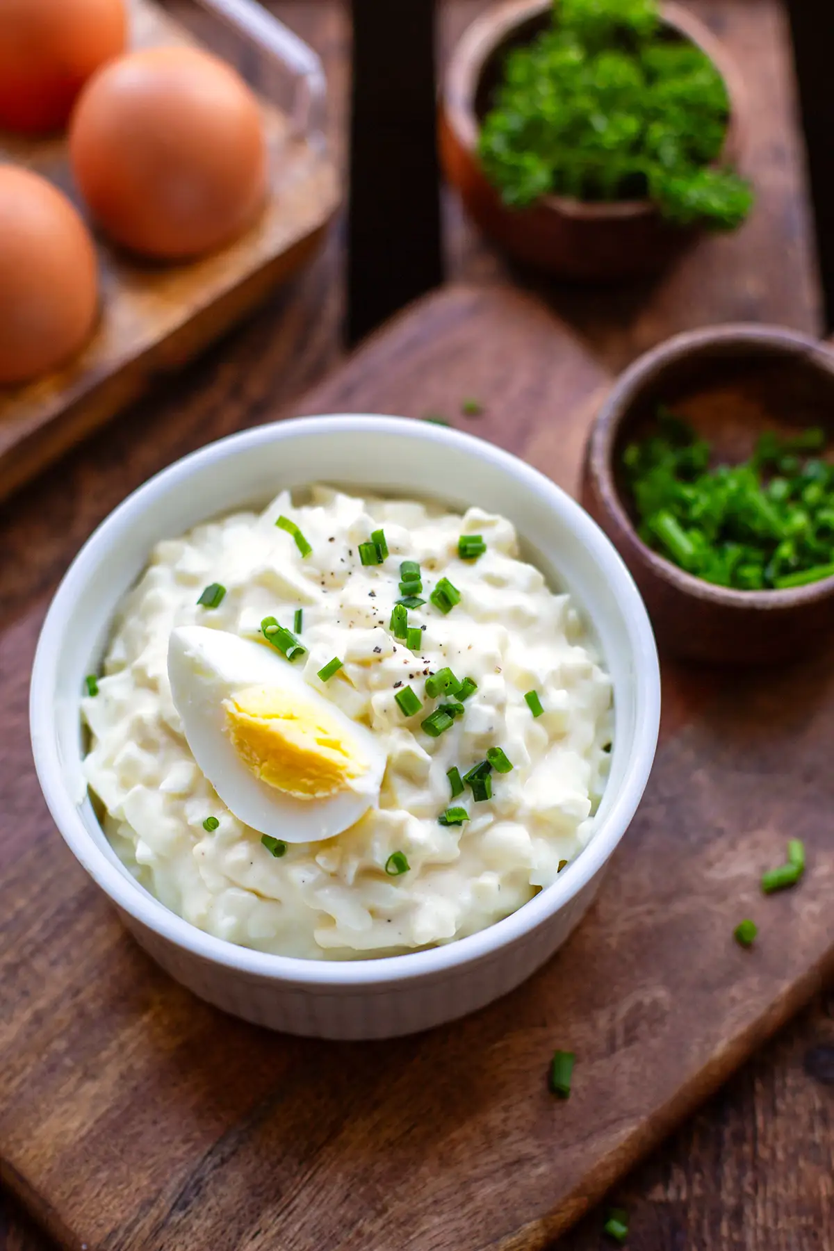 Klassischer Eiersalat wie von Oma angerichtet in einer weißen Schüssel bestreut mit Schnittlauch und Pfeffer, Garniert mit einem hart gekochten Ei.
