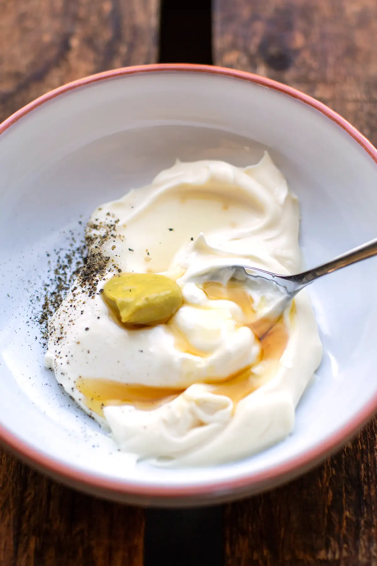 Das Dressing für den Eiersalat in einer weißen Steingut Schale vor dem Verrühren aller Zutaten mit einem Löffel.