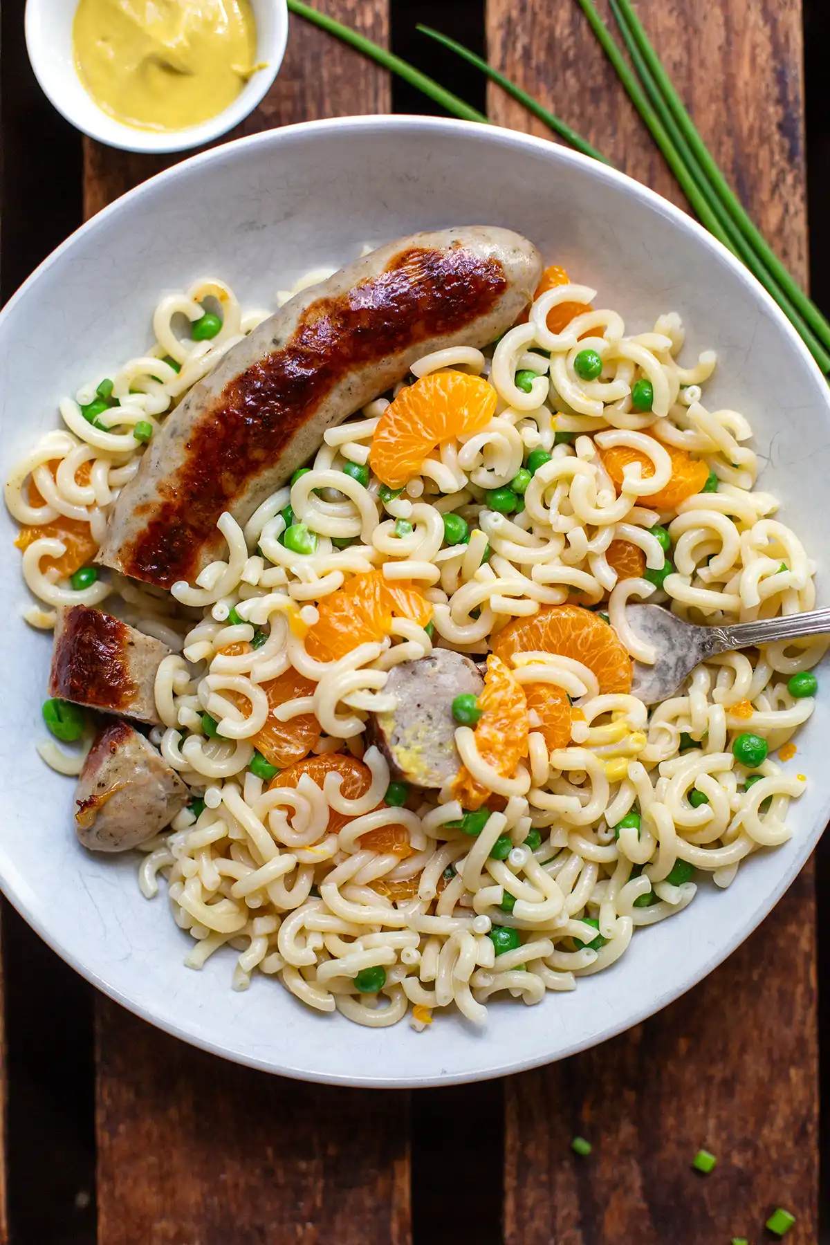 Portion Nudelsalat mit Mandarinen und Erbsen, serviert mit einer gegrillten Bratwurst