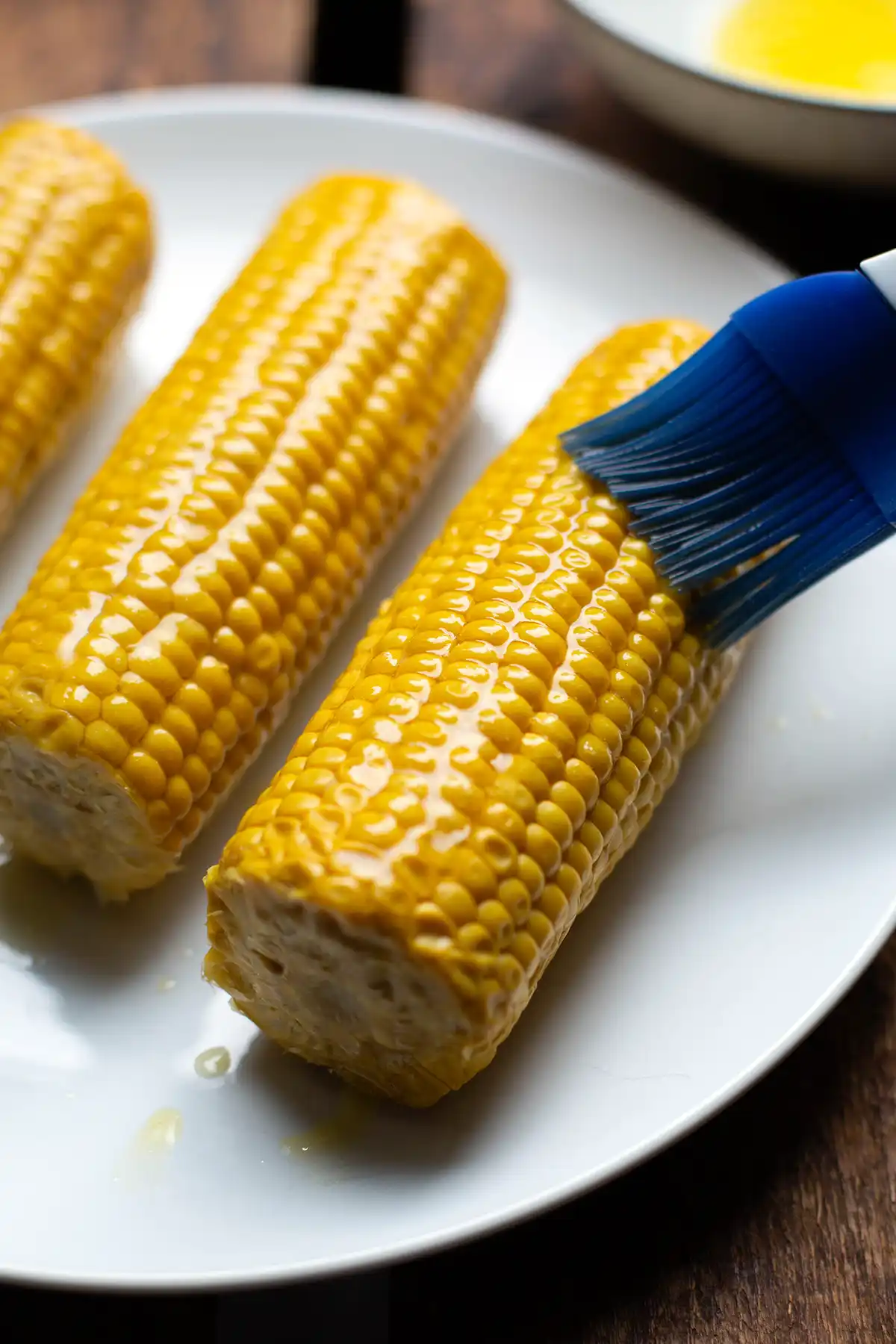 Ein Maiskolben wird mit einem Pinsel gründlich mit geschmolzener Butter bestrichen, bevor er in die Heißluftfritteuse kommt