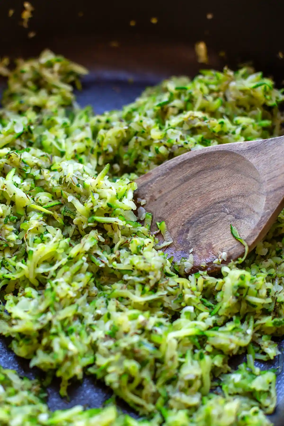 Geraspelte und in einem Küchentuch ausgedrückte Zucchini werden in der Pfanne angebraten