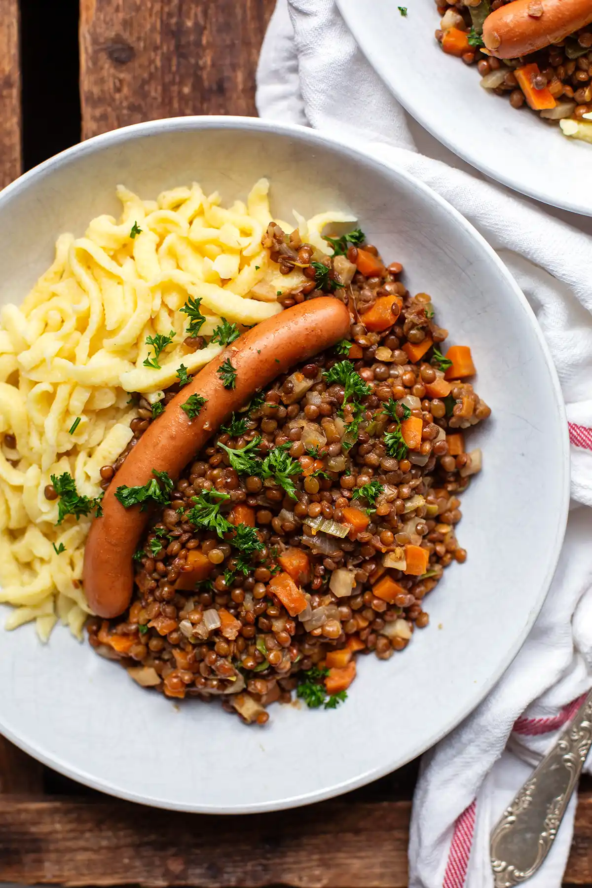 Eine Portion Linsen mit Spätzle und Saitenwürstchen auf einem weißen Teller
